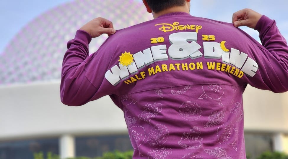 Person in exclusive 2025 runDisney Wine & Dine Half Marathon merchandise poses before a dome-shaped building.