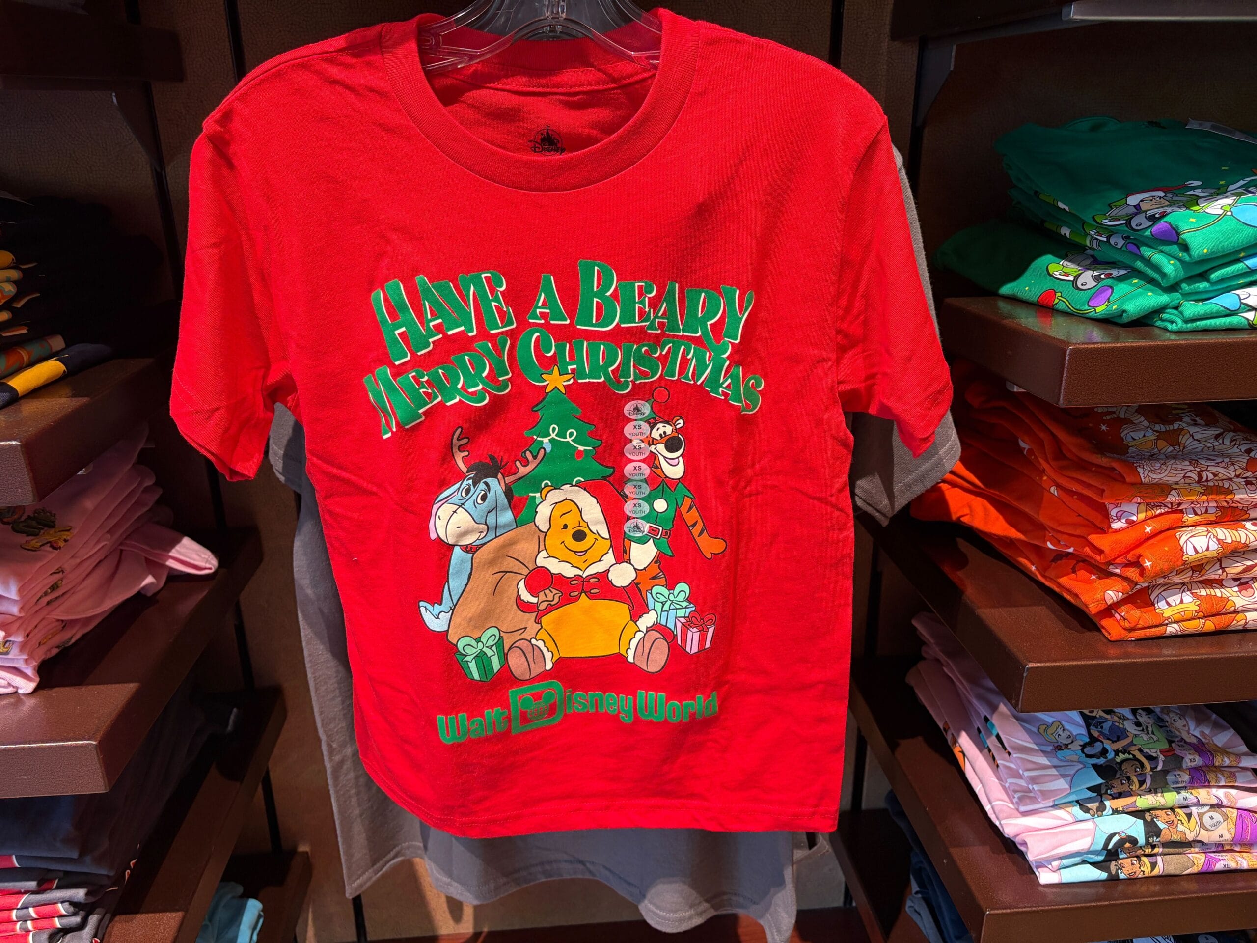 Red Christmas t-shirt with Winnie the Pooh characters and "Have a Beary Merry Christmas" text displayed on a store rack.