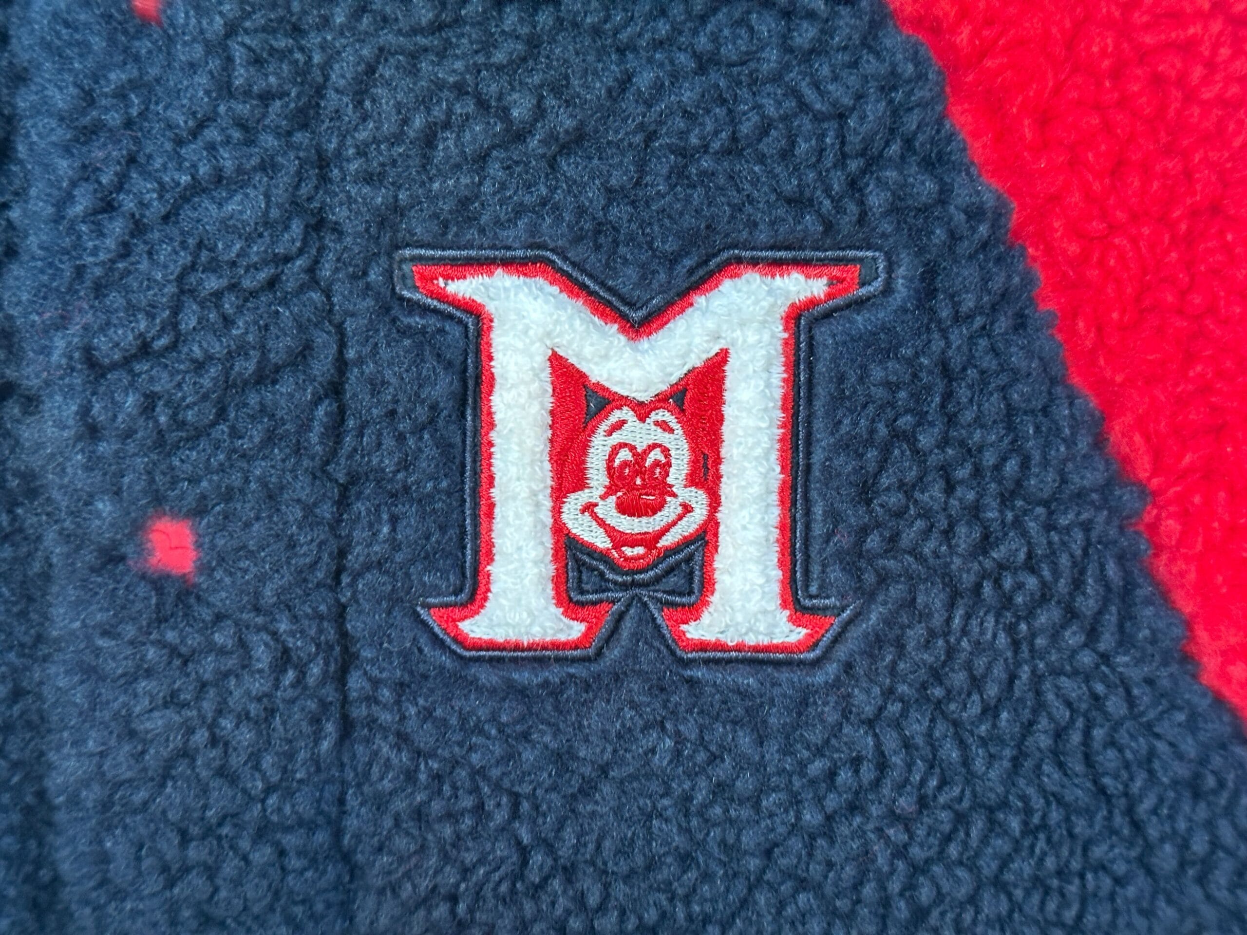 Red and white "M" with Mickey’s face inside, marking Mickey Mouse Club 70th Collection on fabric, reminiscent of Disney Parks merch.