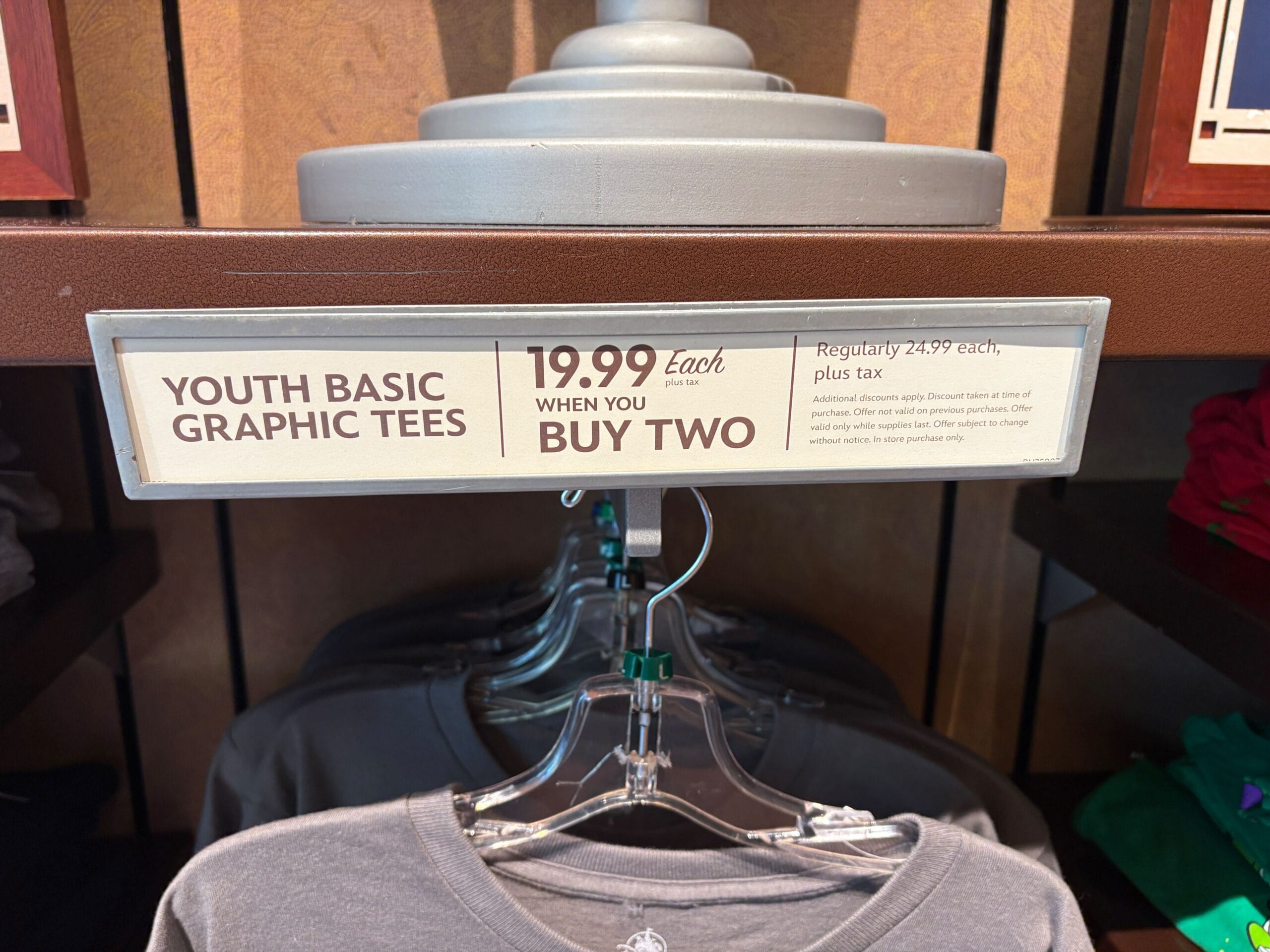 Sign advertising "Youth Basic Graphic Tees: 19.99 each when you buy two, regularly 24.99 each, plus tax.