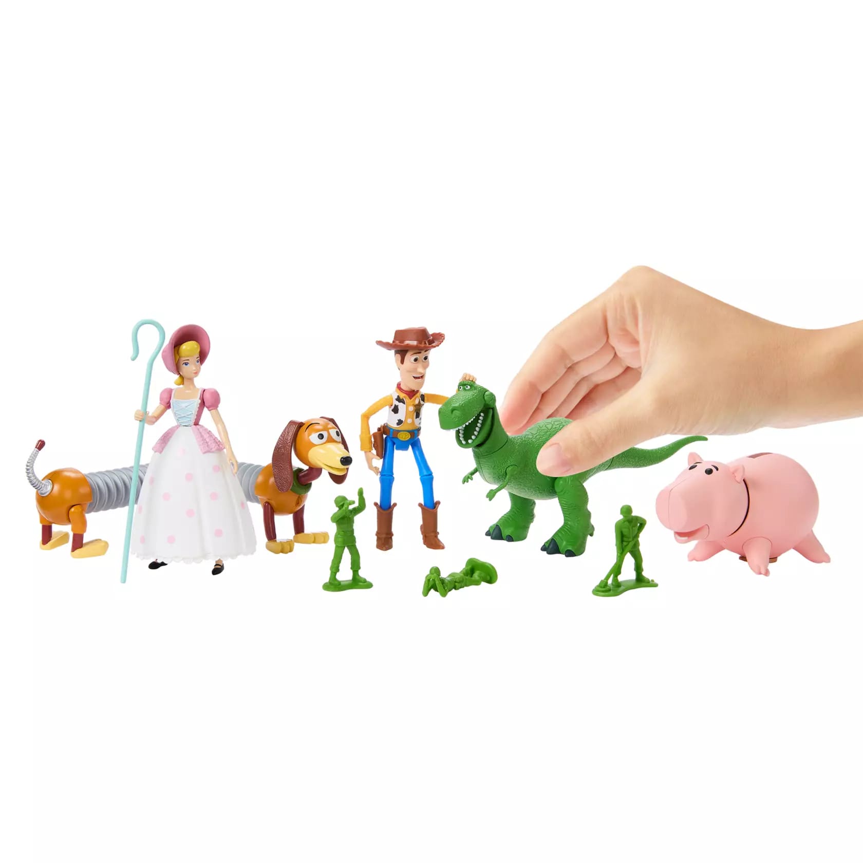 A hand arranges Disney Store Toy Story 30th Anniversary figurines—Woody, Bo Peep, Hamm, Slinky Dog, Rex, and three Green Army Men.