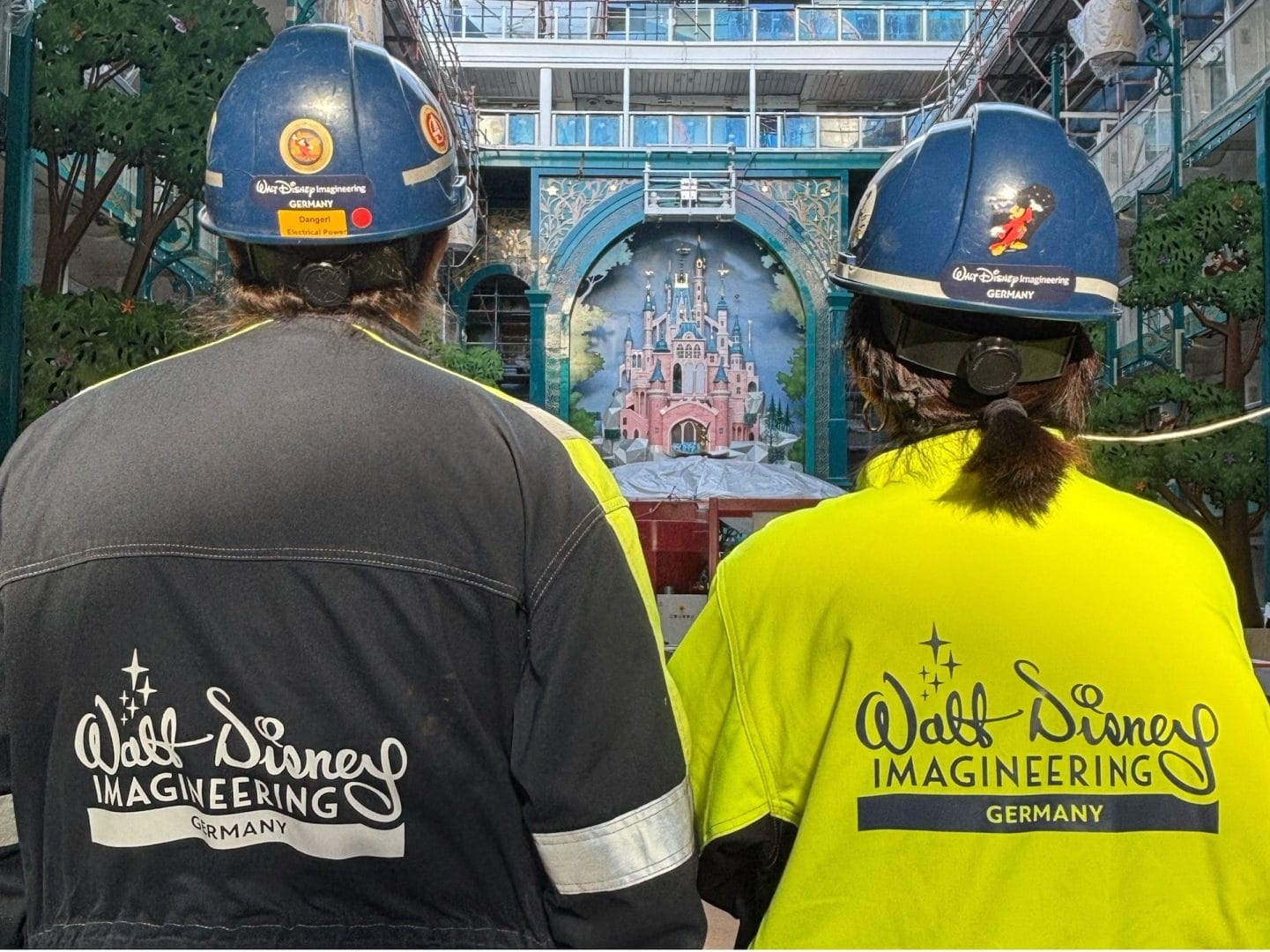 Two in Imagineering Germany gear gaze at an indoor mural of a castle resembling Disneyland Paris more than Cinderella Castle.