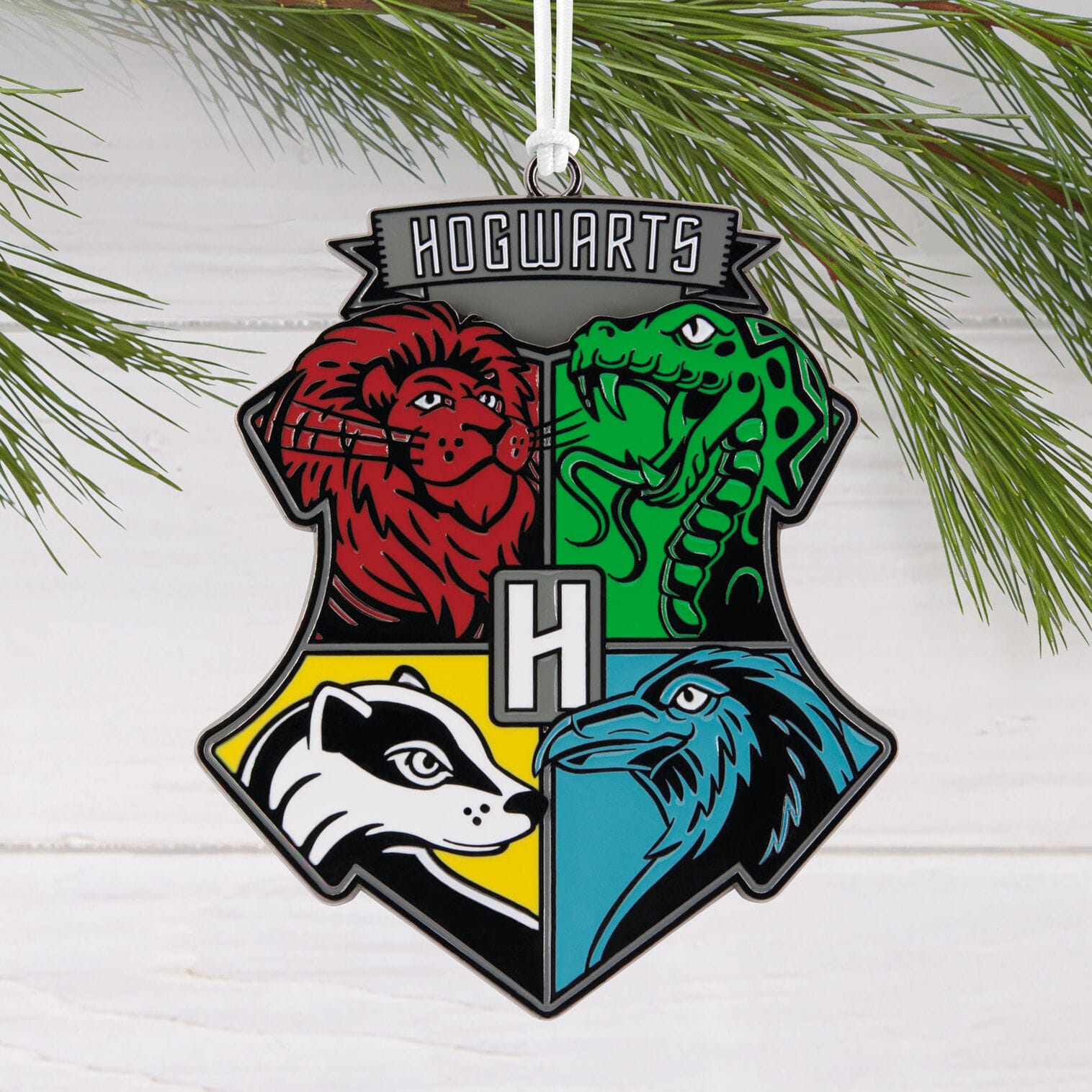 A Hogwarts crest ornament with four house animals hangs on a pine branch