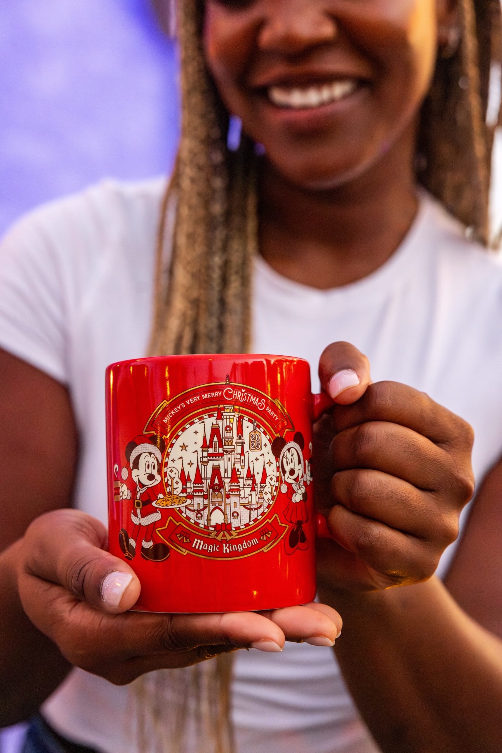 Smiling woman holds a red mug featuring a Magic Kingdom Christmas design from Mickey's Very Merry Christmas Party at Walt Disney World.