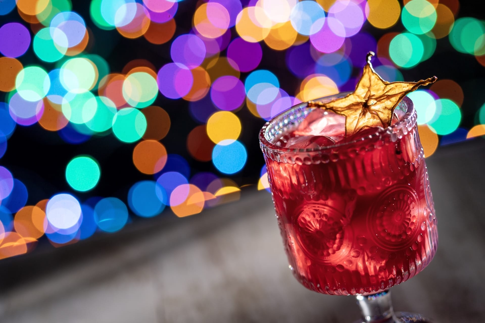 Red cocktail with ice and starfruit garnish for Disney Jollywood Nights 2025, vibrant bokeh reminiscent of Disney park nightlife.