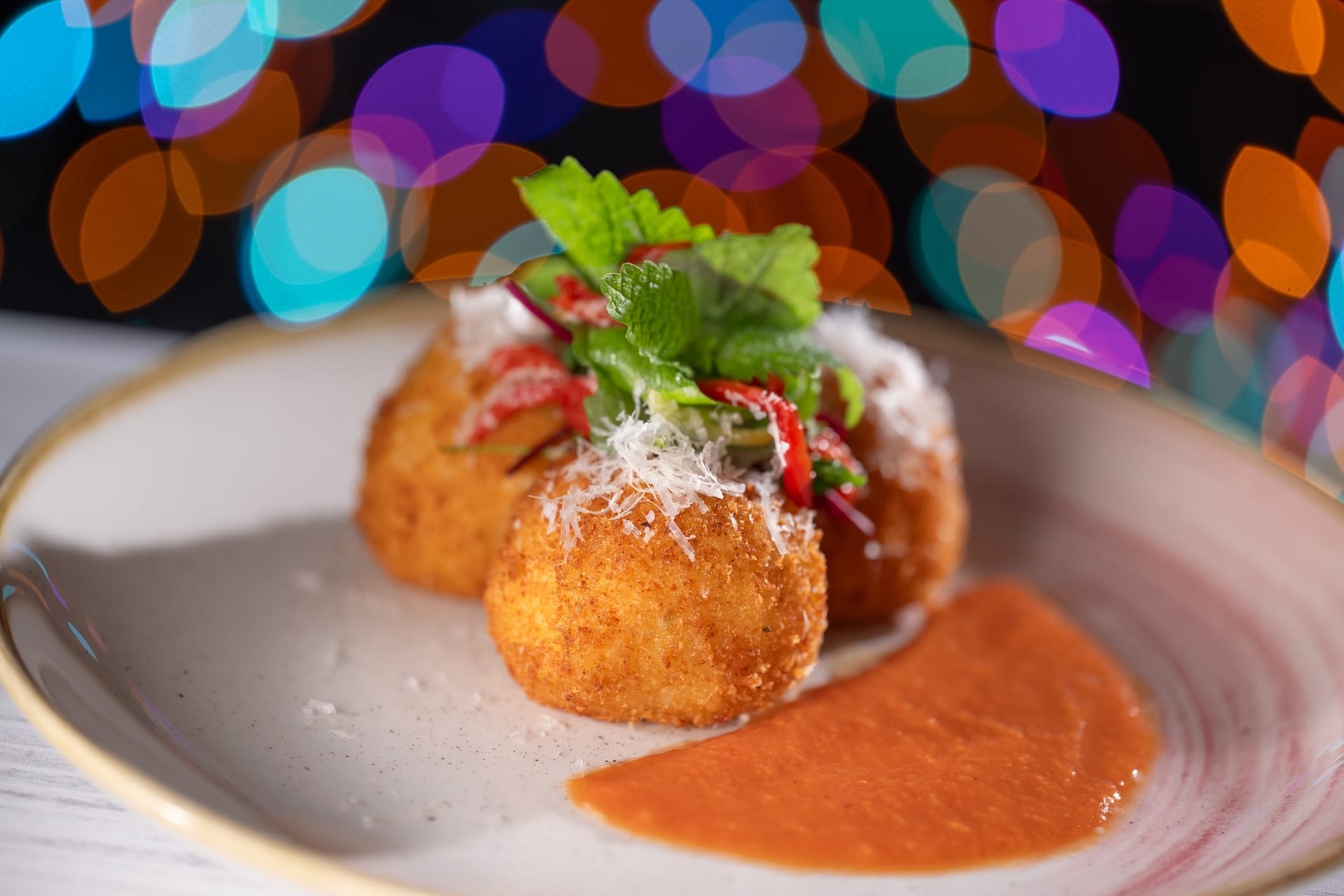 Golden fried arancini with cheese and tomato sauce at Disney Jollywood Nights 2025, sparkling lights reminiscent of park festivities.