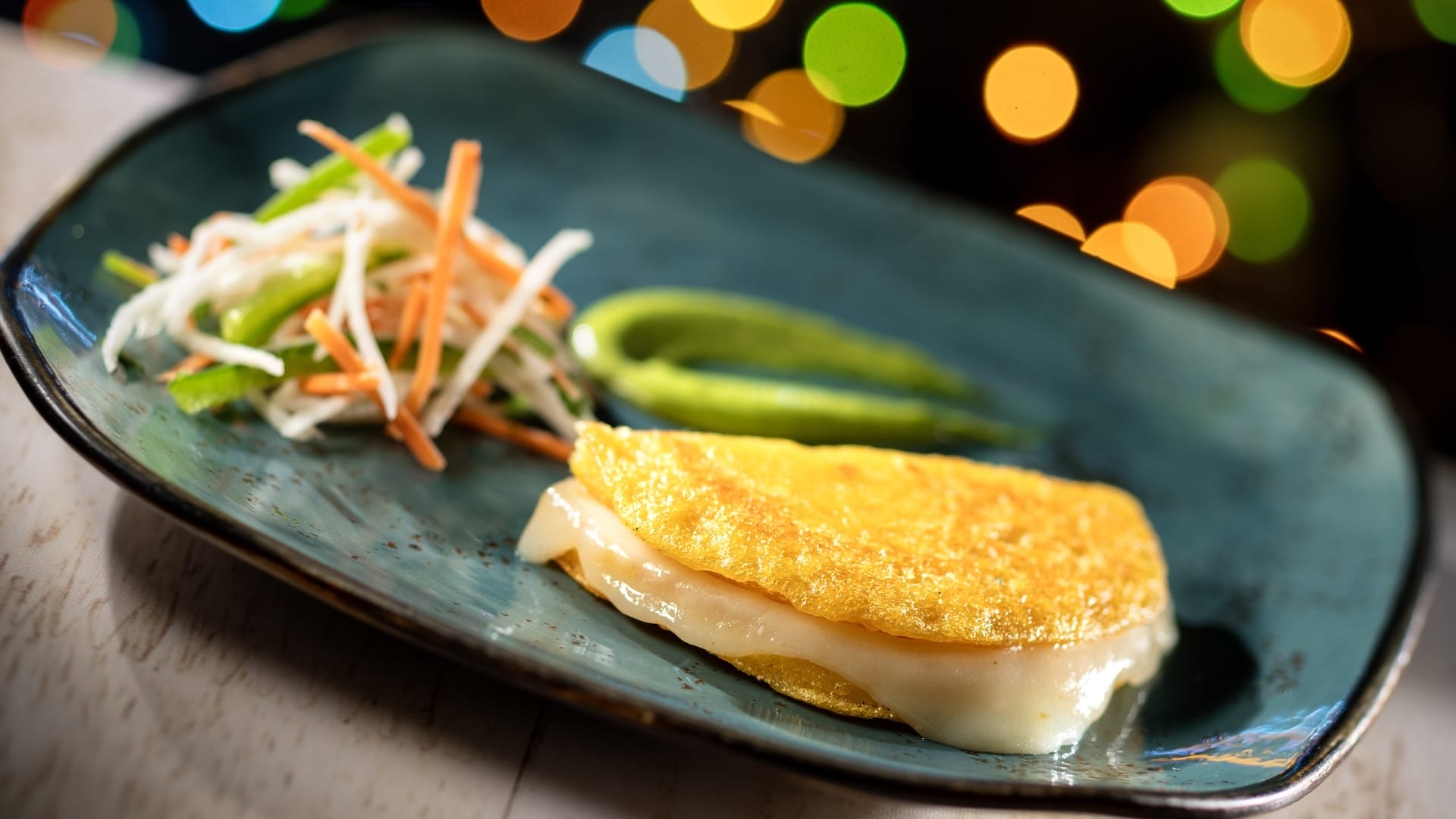 Golden arepa oozing melted cheese, with vibrant slaw and green sauce—2025 Disney Jollywood Nights treat, no castle comparison needed.