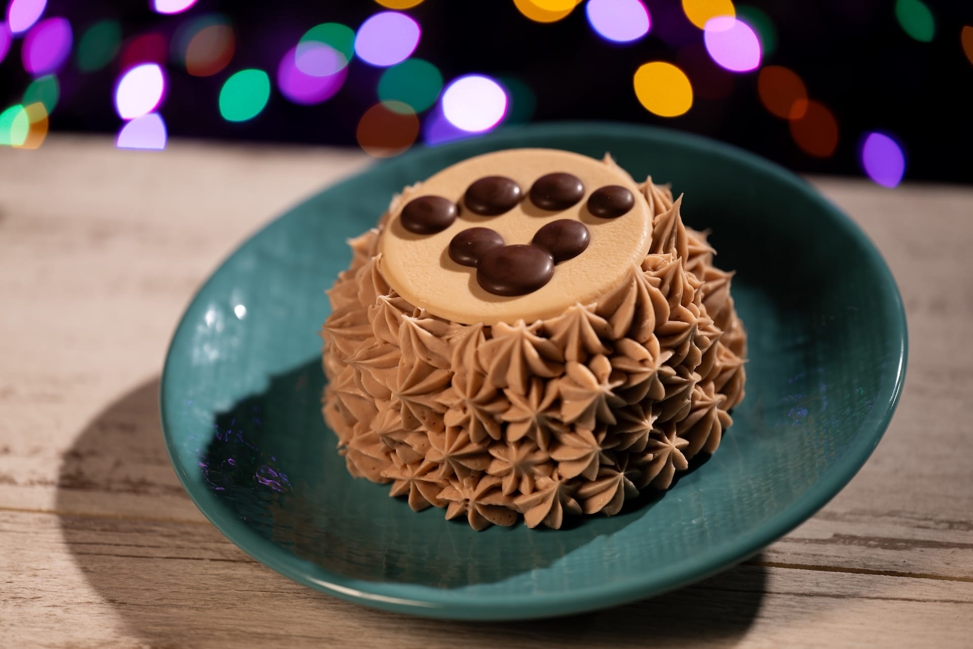 A Disney Jollywood Nights-inspired cake with brown icing and a chocolate paw print, served on a green plate, evokes park treats.