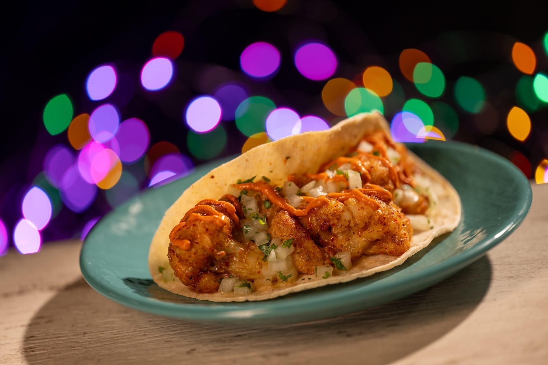 A shrimp taco topped with onions and cilantro on a teal plate at Disney Jollywood Nights 2025, no castle in view.