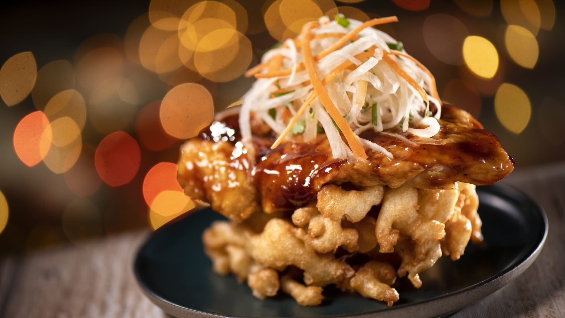 Glazed chicken atop a crispy waffle with veggies on a dark plate, themed after Disney Jollywood Nights 2025 at Walt Disney World.