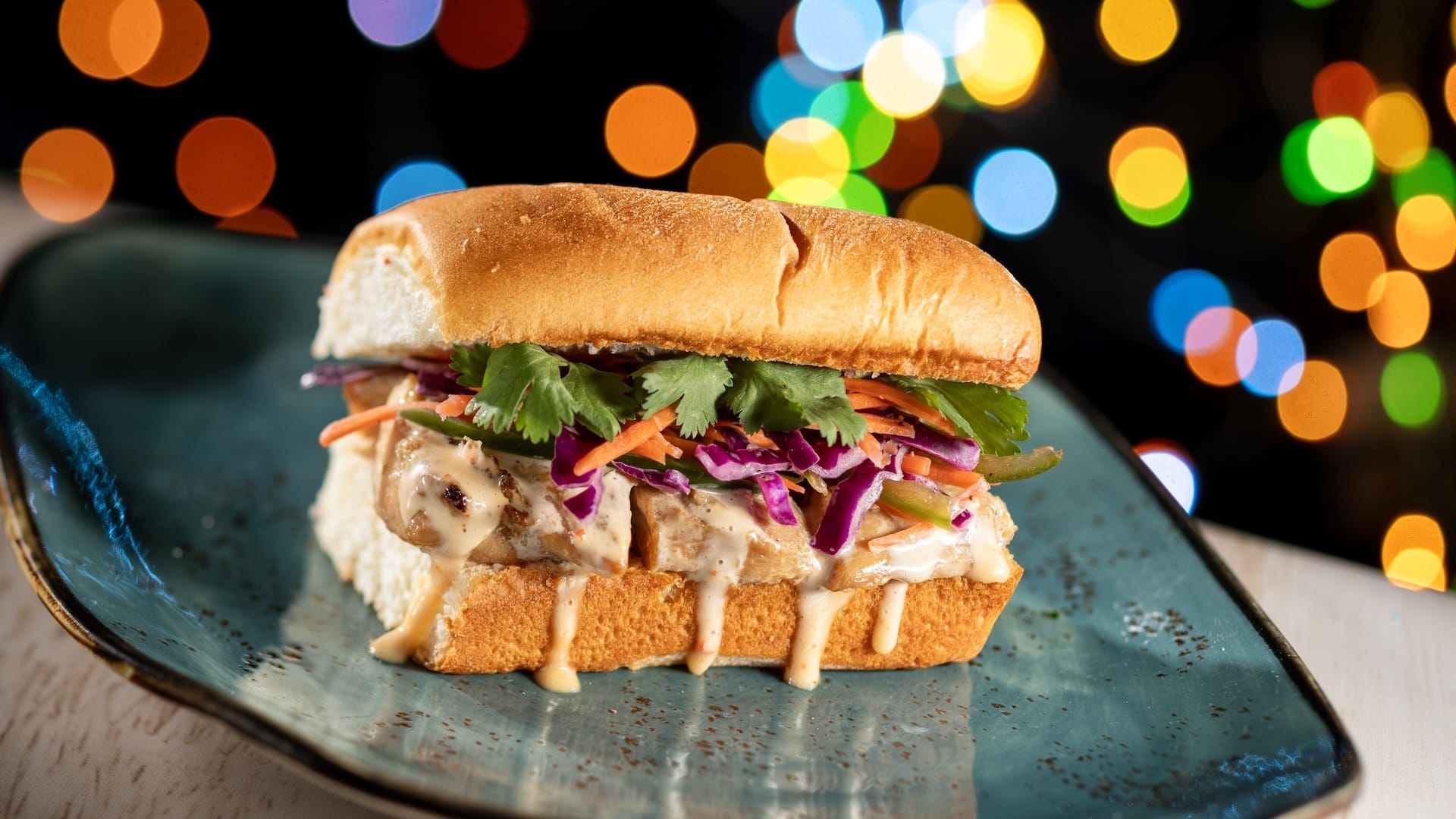 Grilled chicken and veggie sandwich inspired by Disney Jollywood Nights, served on a plate amid colorful theme park lights.