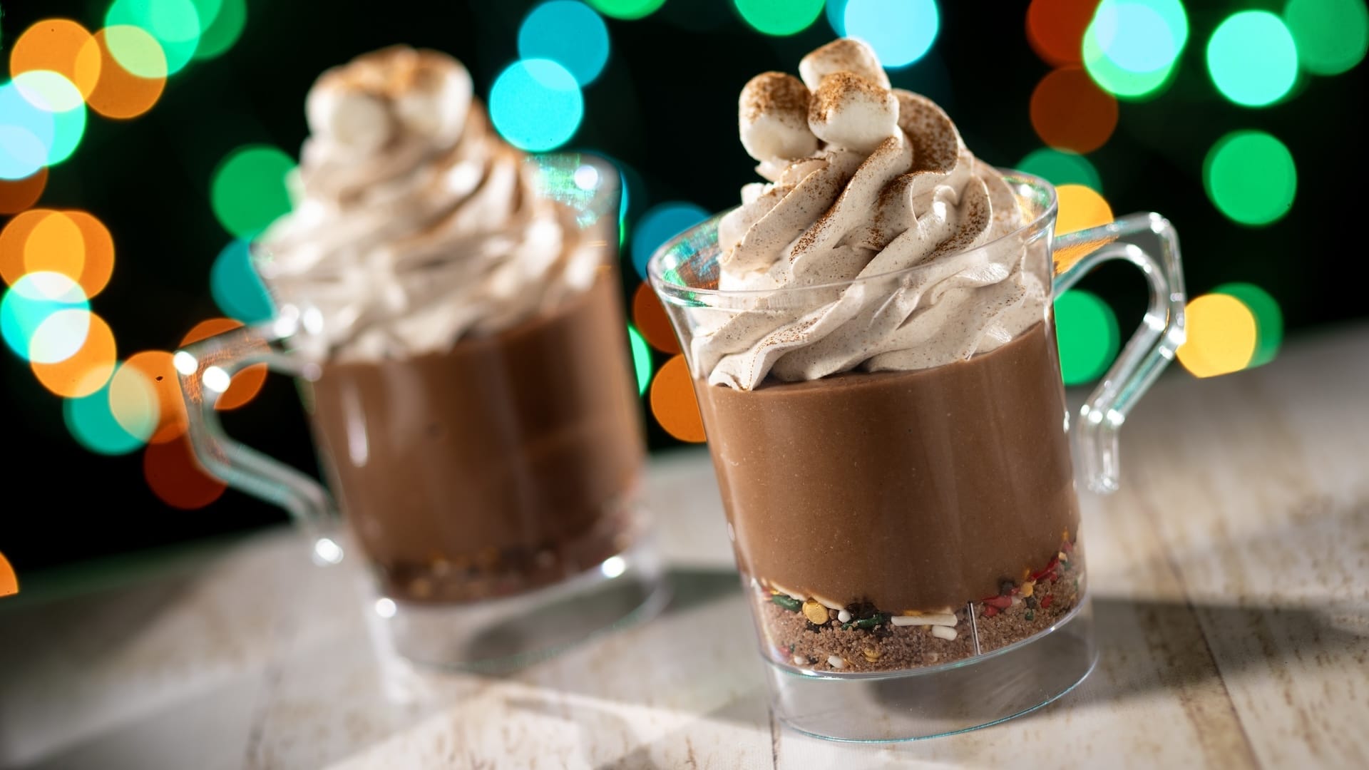 Two clear mugs of chocolate mousse topped with whipped cream and marshmallows, themed for 2025 Disney Jollywood Nights event.