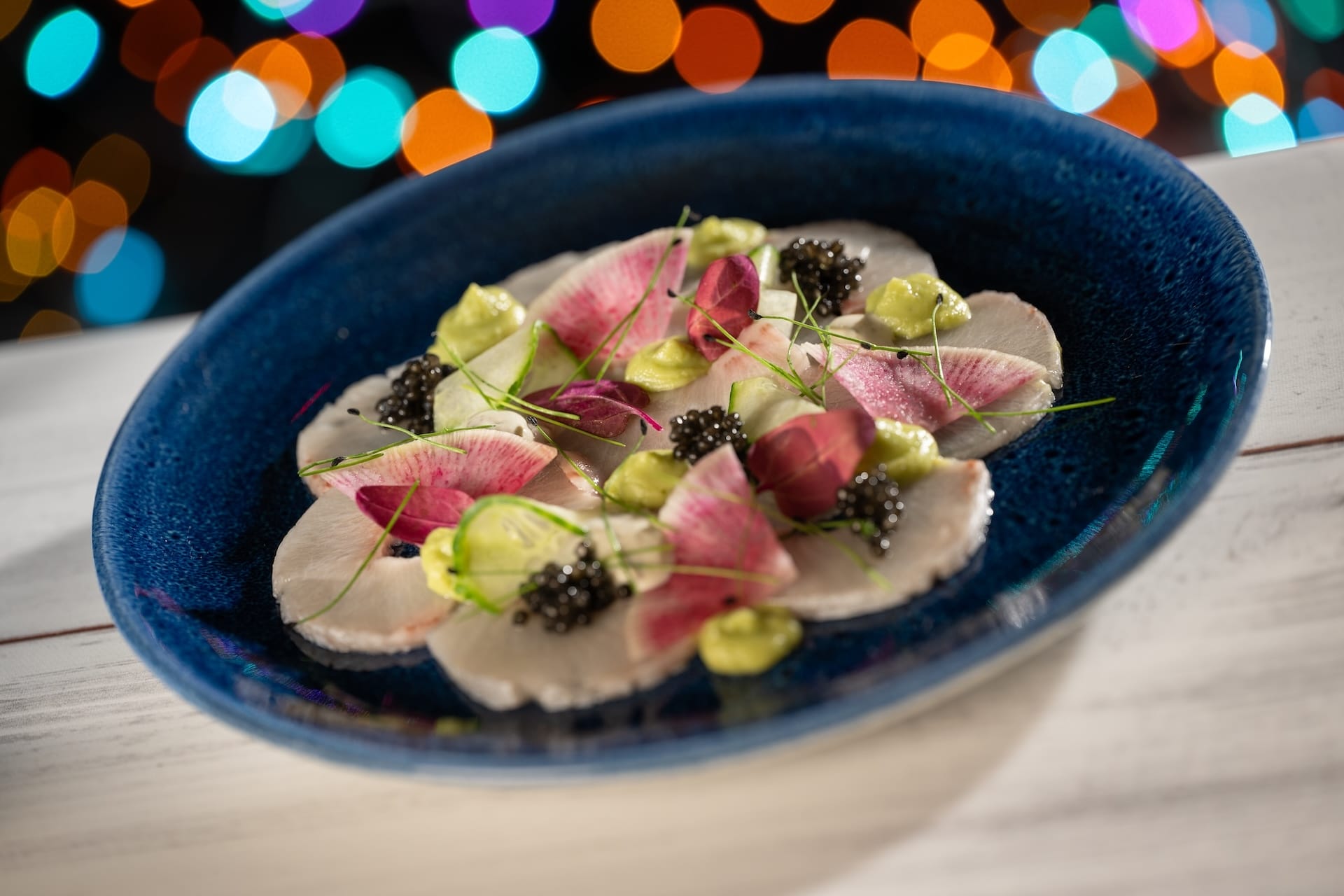 A blue plate with sliced radishes, green sauce, and caviar—Disney Jollywood Nights 2025 specialty, no castle in view.
