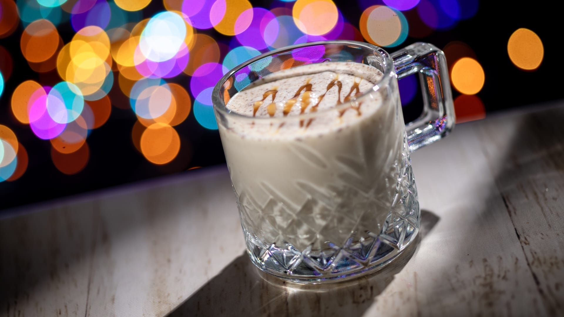 A glass mug of creamy drink topped with caramel drizzle, one of the new 2025 Disney Jollywood Nights treats at Walt Disney World.