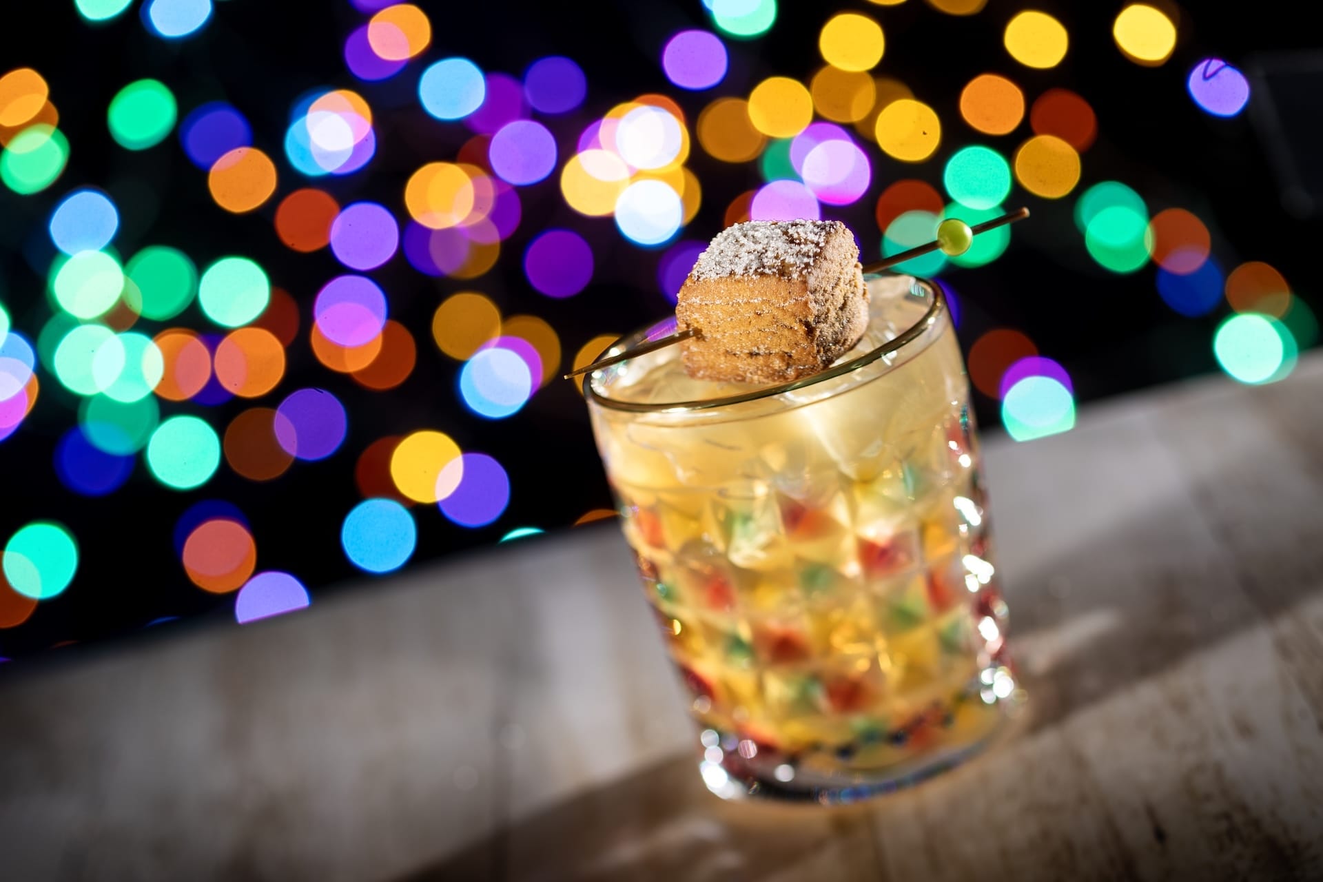 A Disney Jollywood Nights cocktail in a textured glass with a powdered pastry garnish, showcasing festive park-exclusive treats.