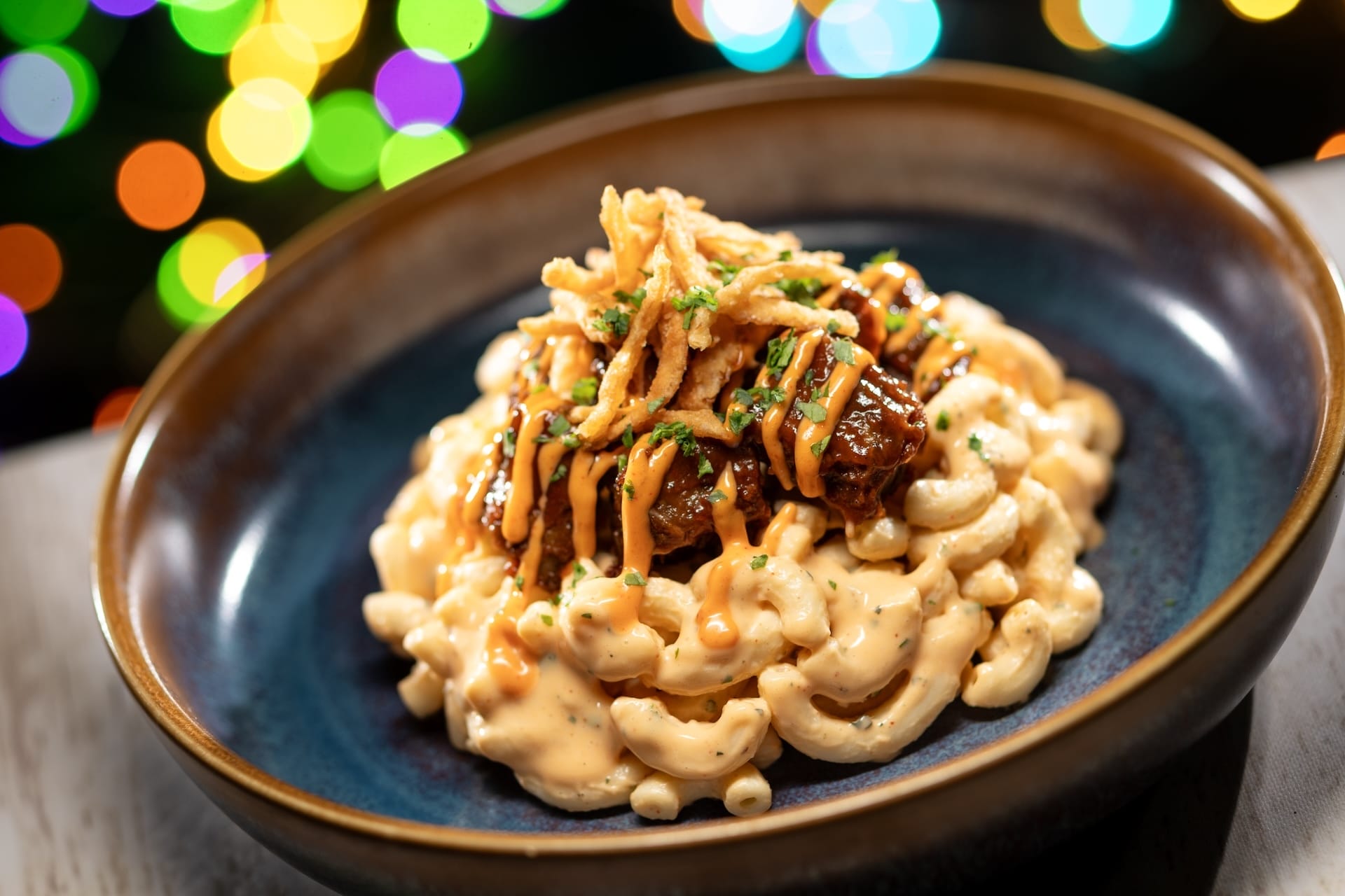 Savor 2025 Disney Jollywood Nights mac and cheese topped with saucy meat, crispy onions, and zesty orange sauce—no castle in view.
