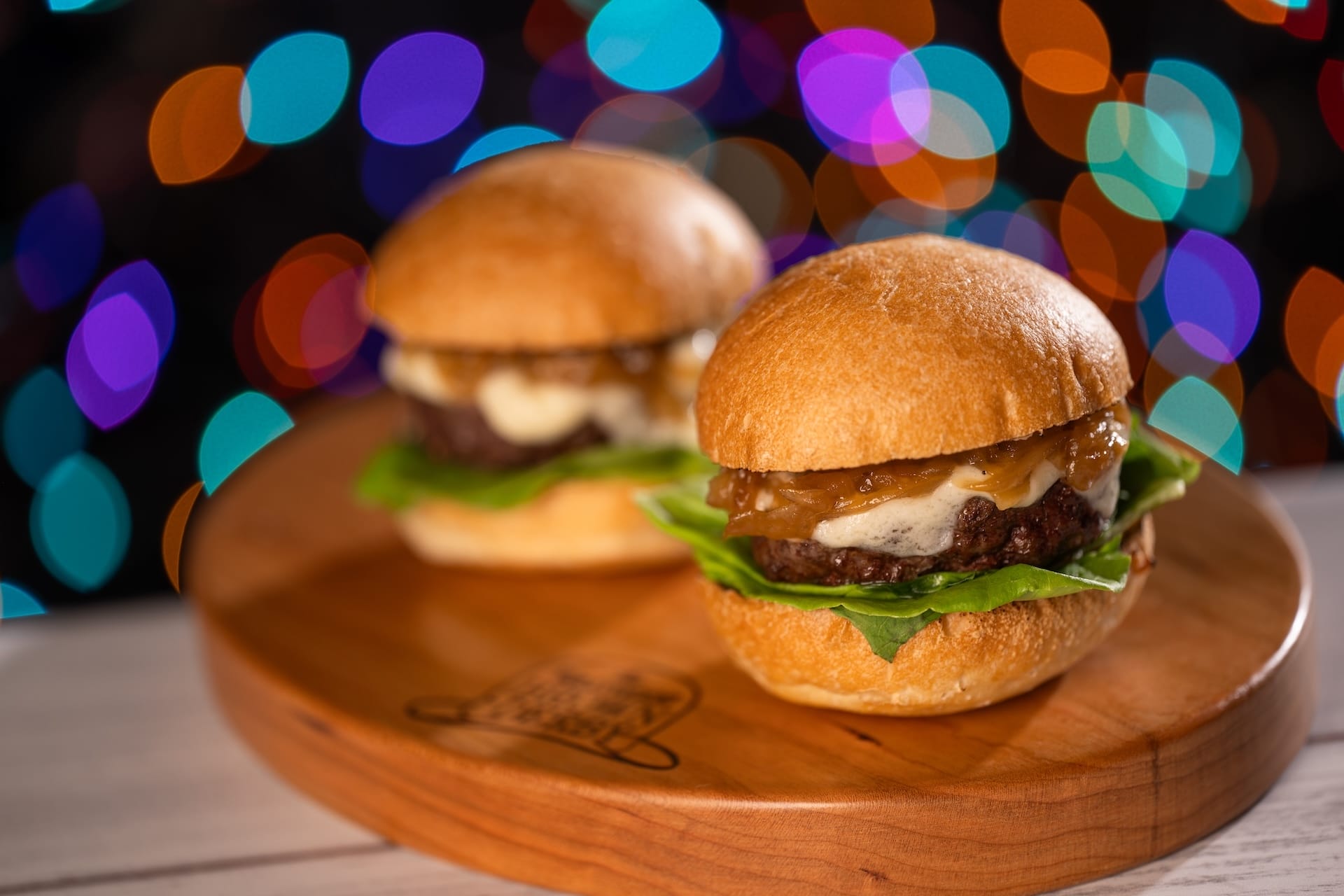 Two gourmet burgers with lettuce and caramelized onions served at Disney Jollywood Nights, styled on a board, dreamy background.