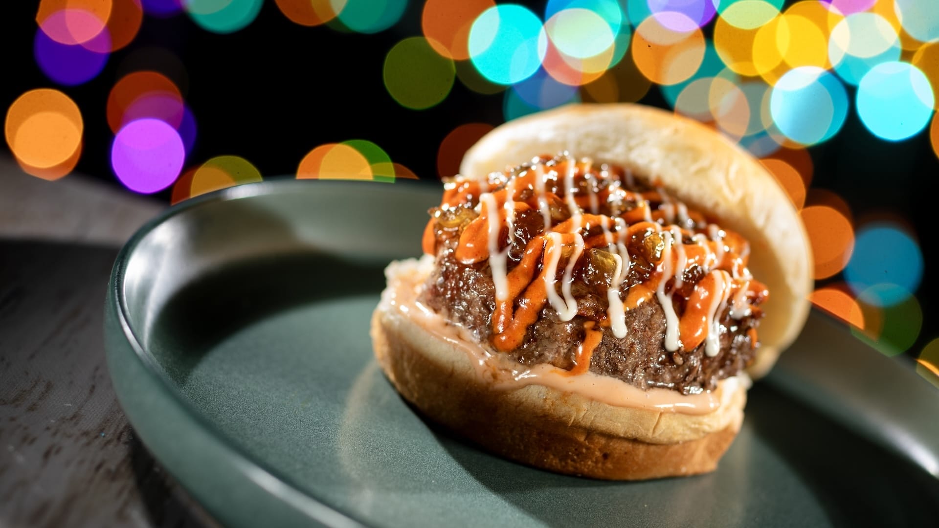 A burger topped with sauce on a green plate, featured in Disney Jollywood Nights 2025 new menu at Walt Disney World.
