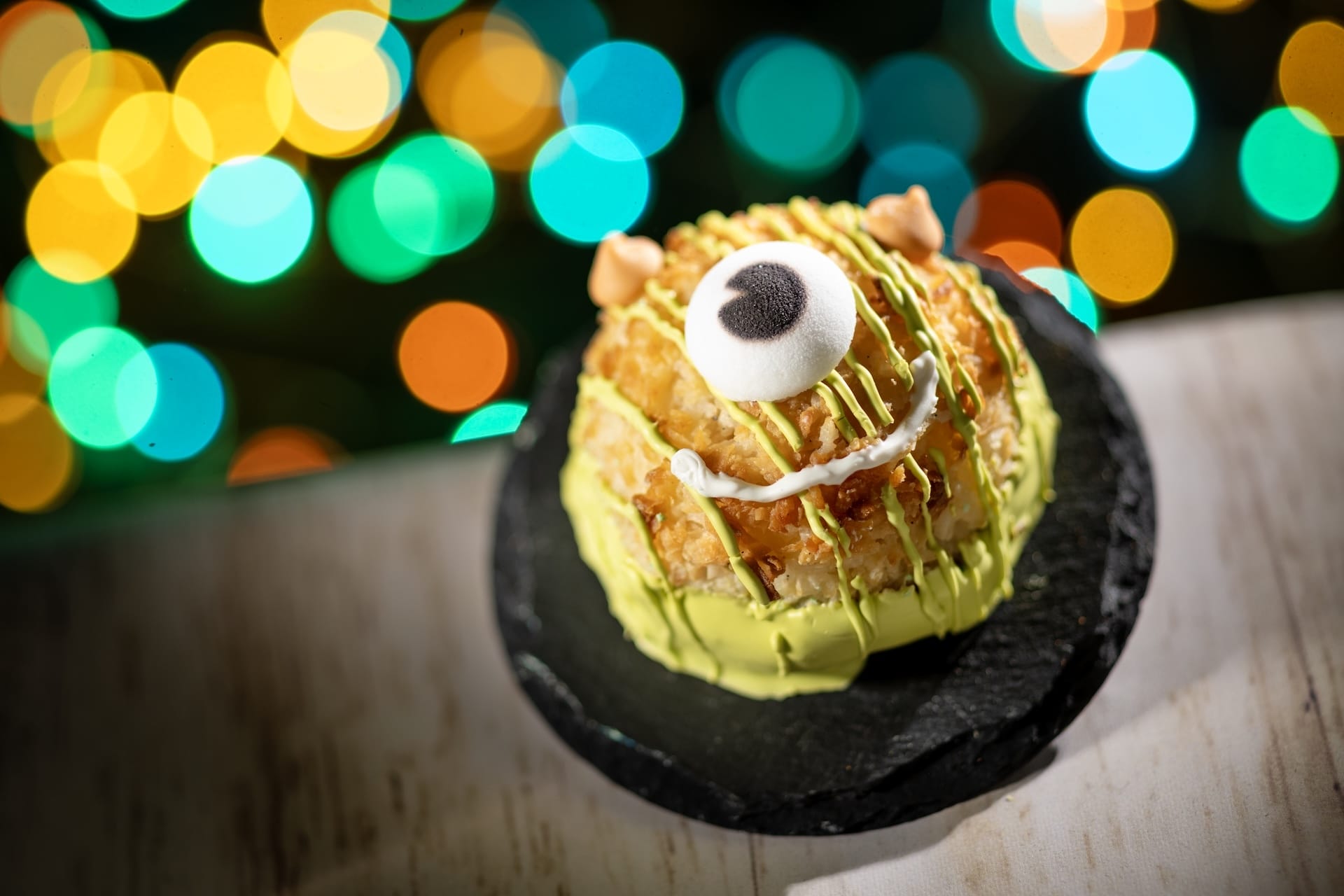 A 2025 Disney Park treat: a pastry with green icing and a marshmallow eye, served on a black plate, perfect for fans.
