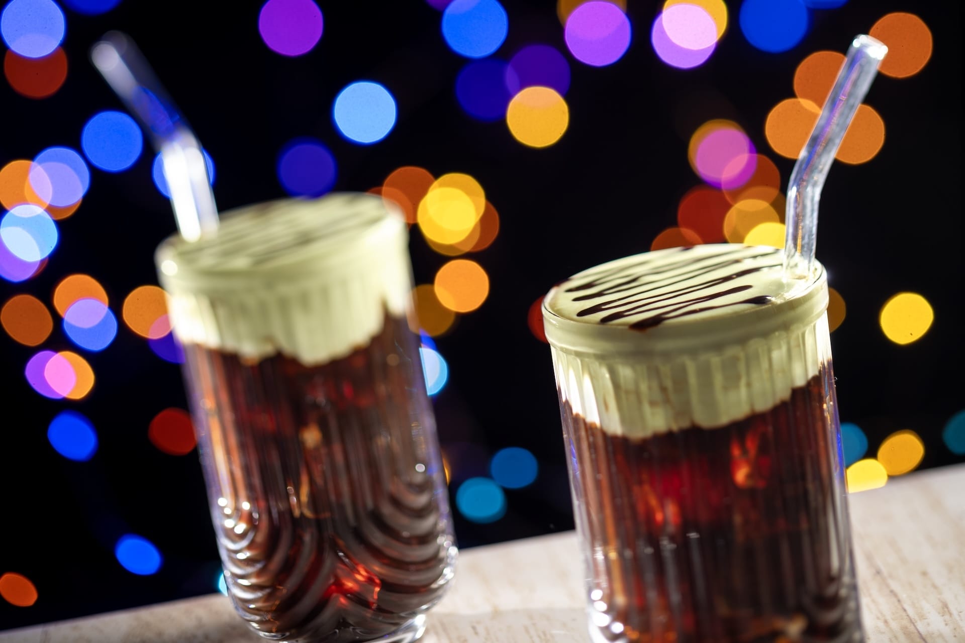 Two glasses of iced coffee with cream and chocolate syrup, set for Disney Jollywood Nights under sparkling park lights.
