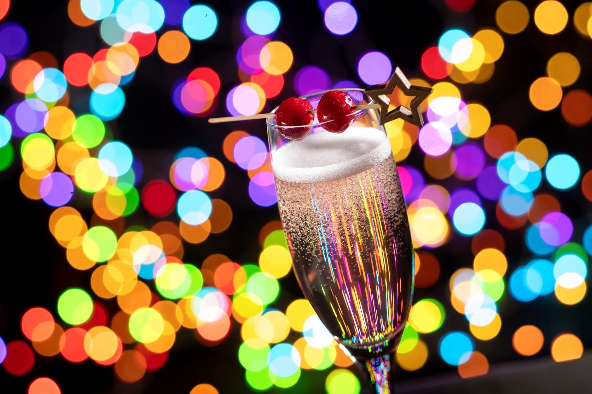 A champagne glass with cherries and star stirrer sparkles amid festive lights at Disney Jollywood Nights 2025—no castle view shown.