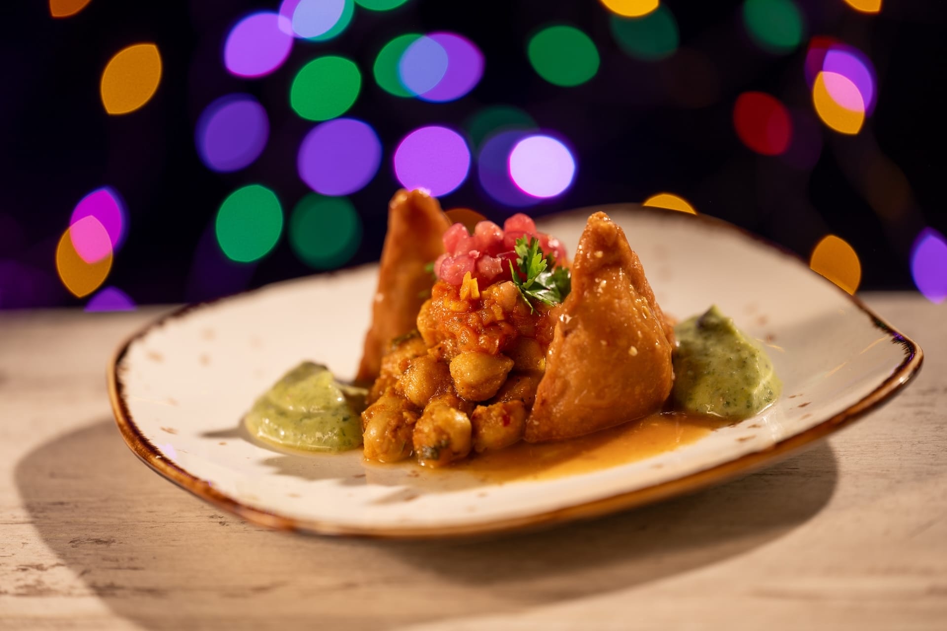 Two samosas with chickpea curry and green chutney on a white plate at Disney Jollywood Nights—no castle like those in Disney Parks.