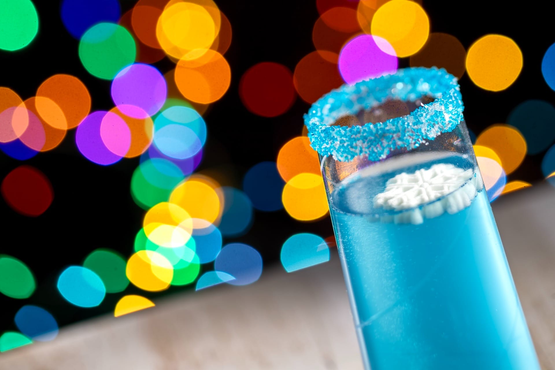 A blue festive drink in a glass with a sugared rim, reminiscent of creative Disney Park beverages, against sparkling bokeh lights.