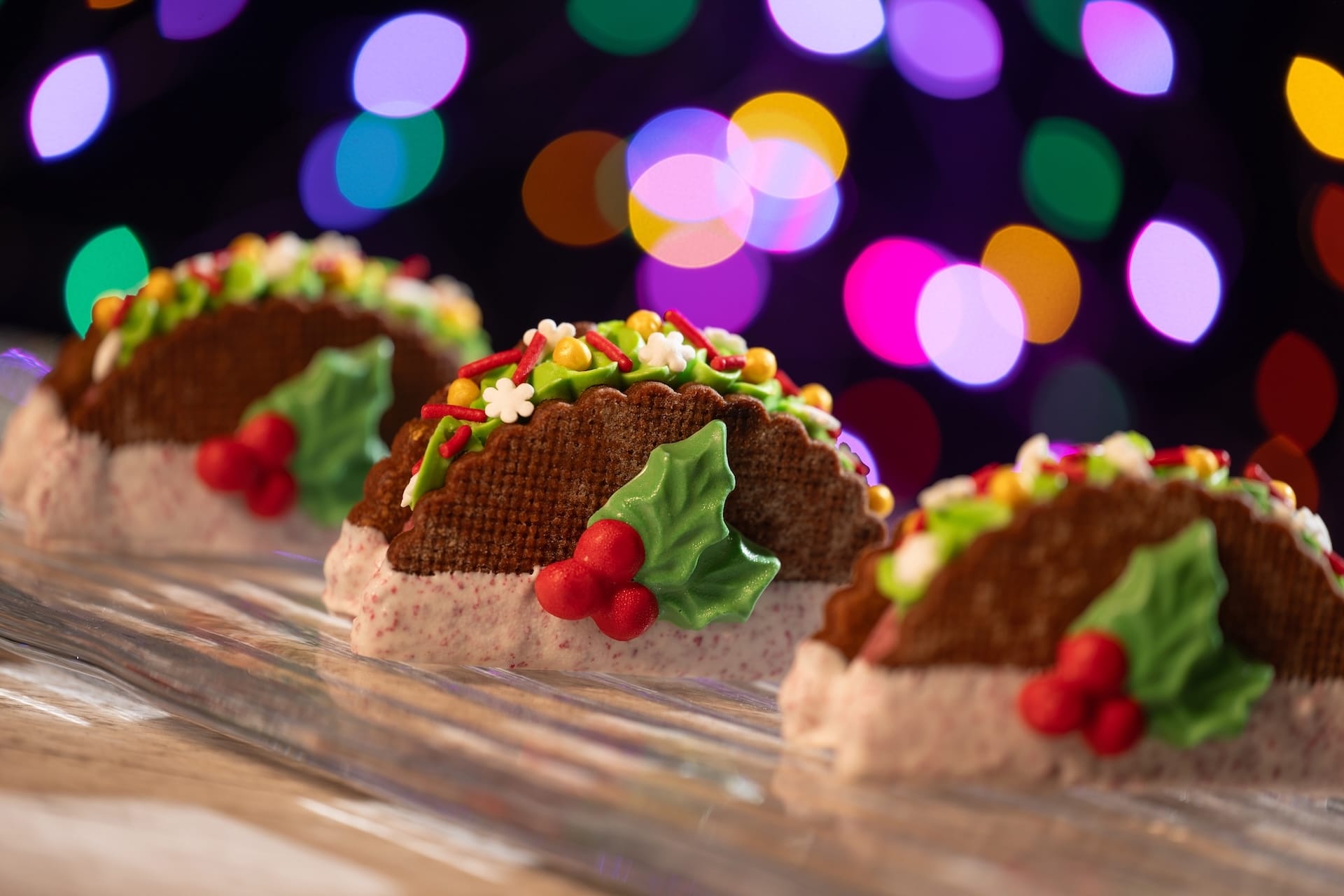 Three festive dessert tacos at Disney Jollywood Nights, with blurred holiday lights like those found at Disney parks worldwide.