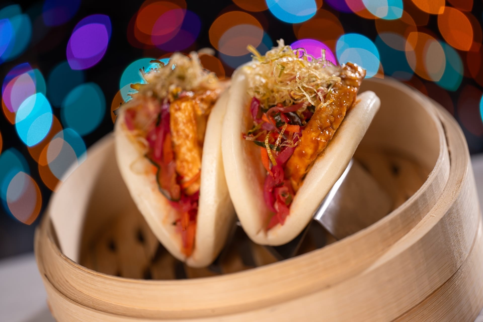 Two bao buns with vibrant fillings in a bamboo steamer, featured as a new treat for Disney Jollywood Nights 2025 at Walt Disney World.