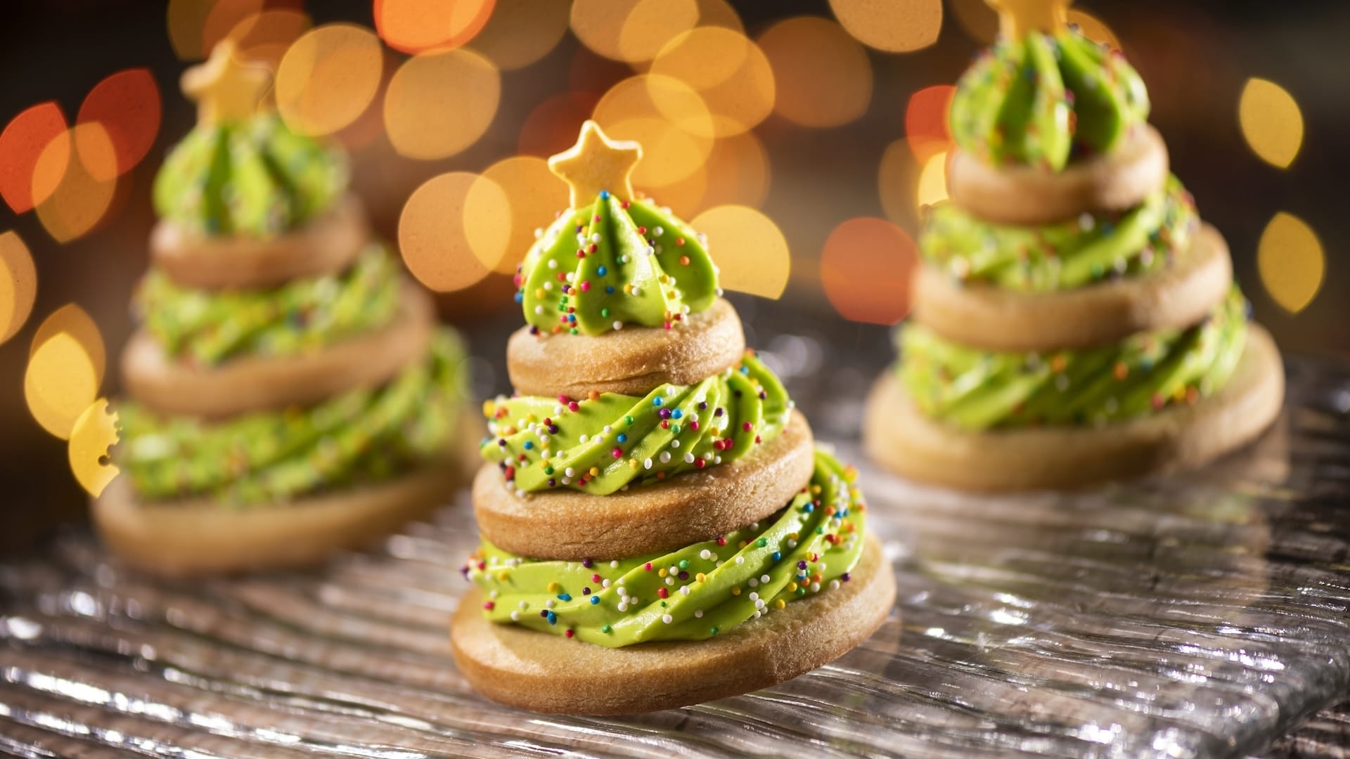 Three Christmas tree cookies with green frosting and festive sprinkles, inspired by Disney Jollywood Nights treats at the parks.