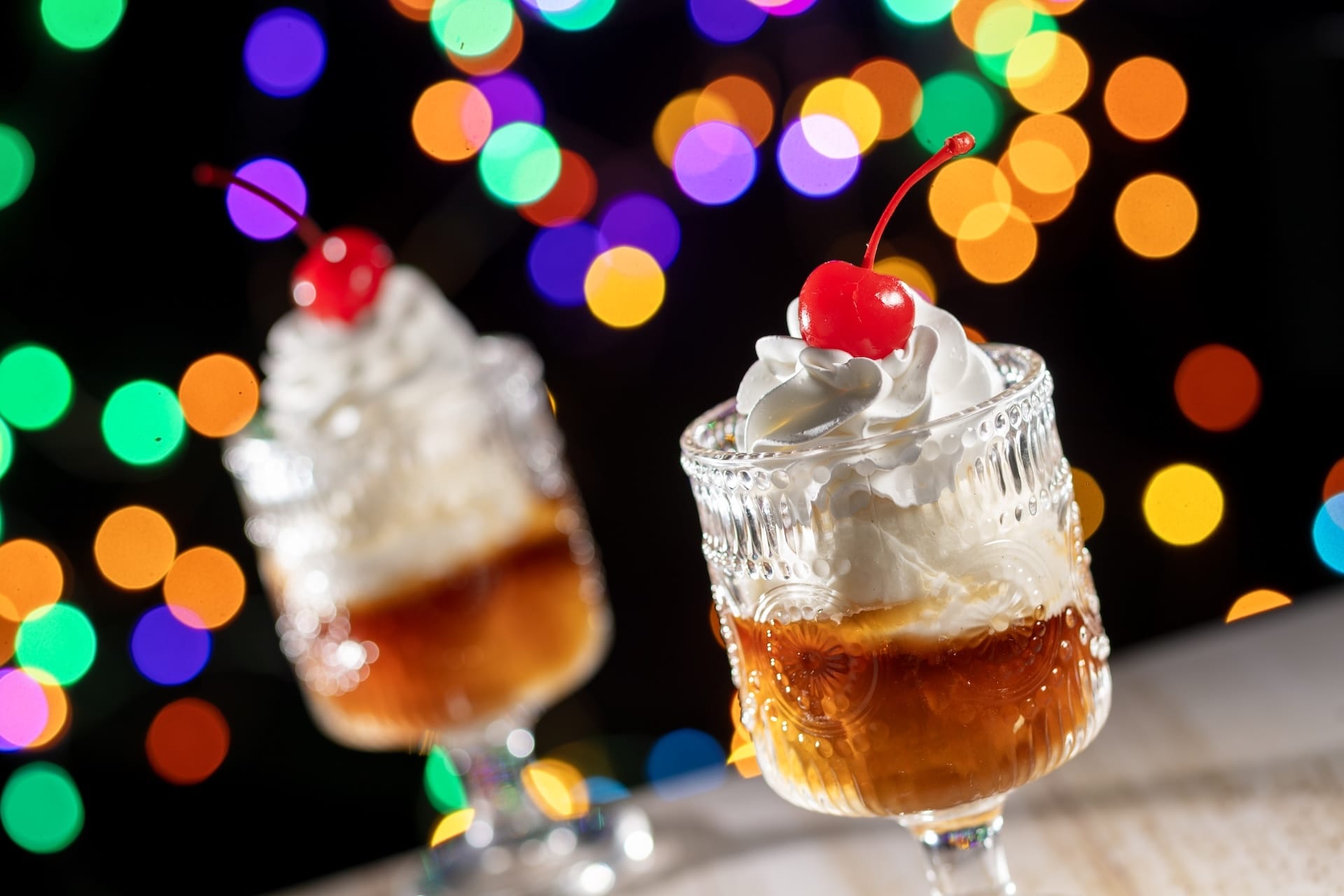 Two elegant dessert glasses topped with whipped cream and cherries, a festive treat for Disney Jollywood Nights at the parks.