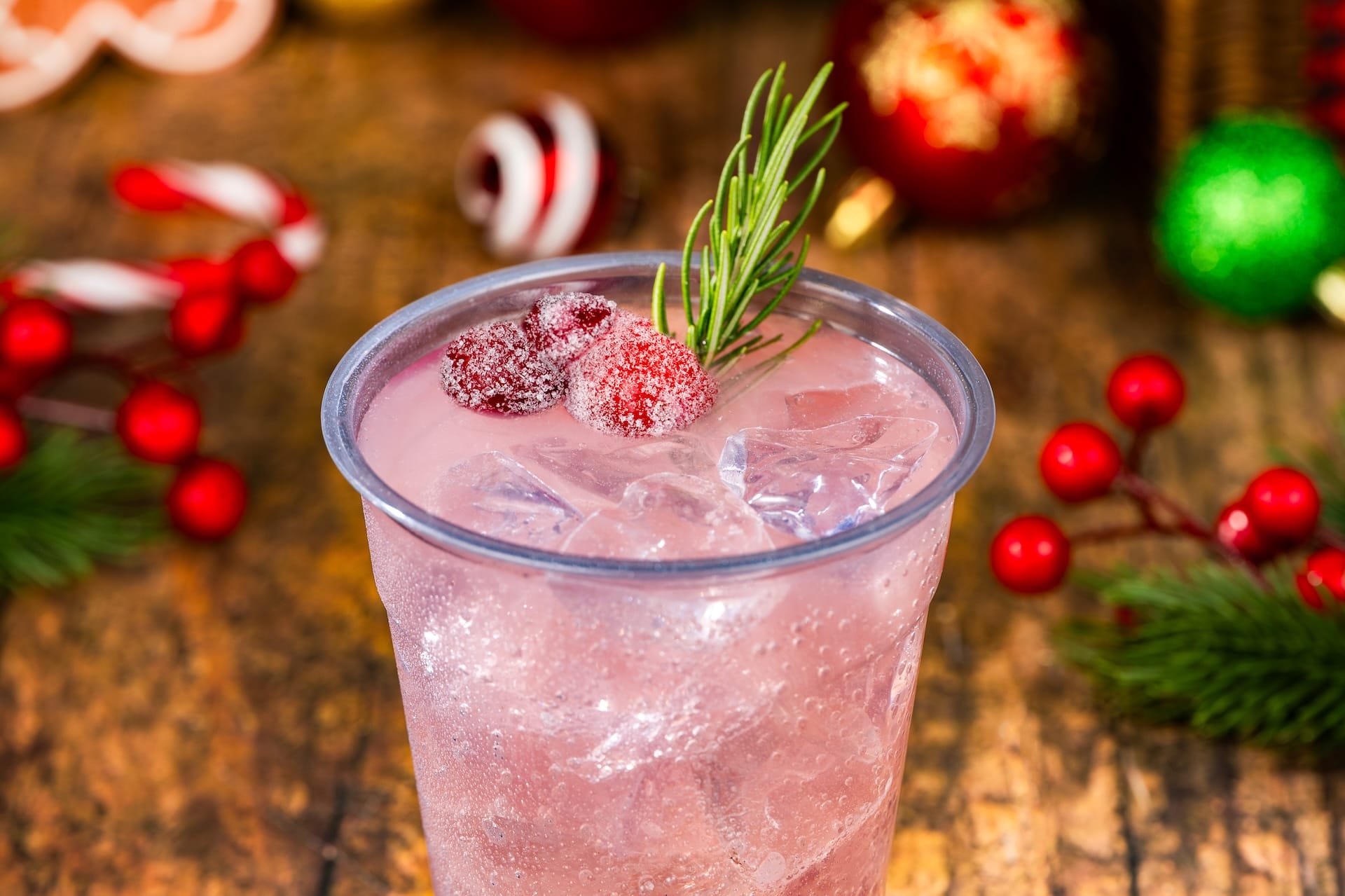 A cheerful pink holiday drink with ice, sugared cranberries, and rosemary for Mickey’s Very Merry Christmas Party at Disney Parks.