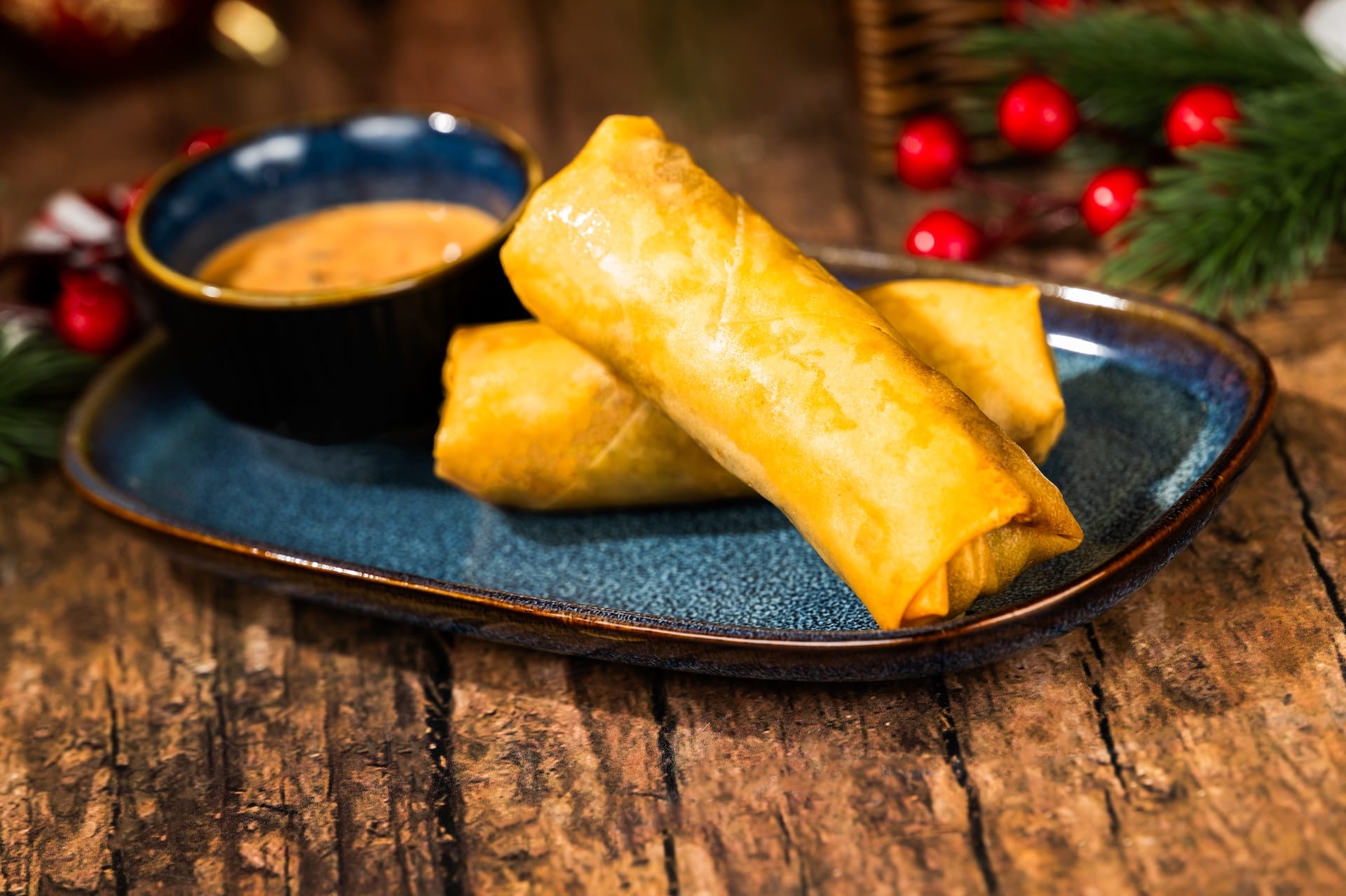 Two golden spring rolls with dipping sauce on a blue plate, Holiday menu item among festive decor, reminiscent of Disney park treats.