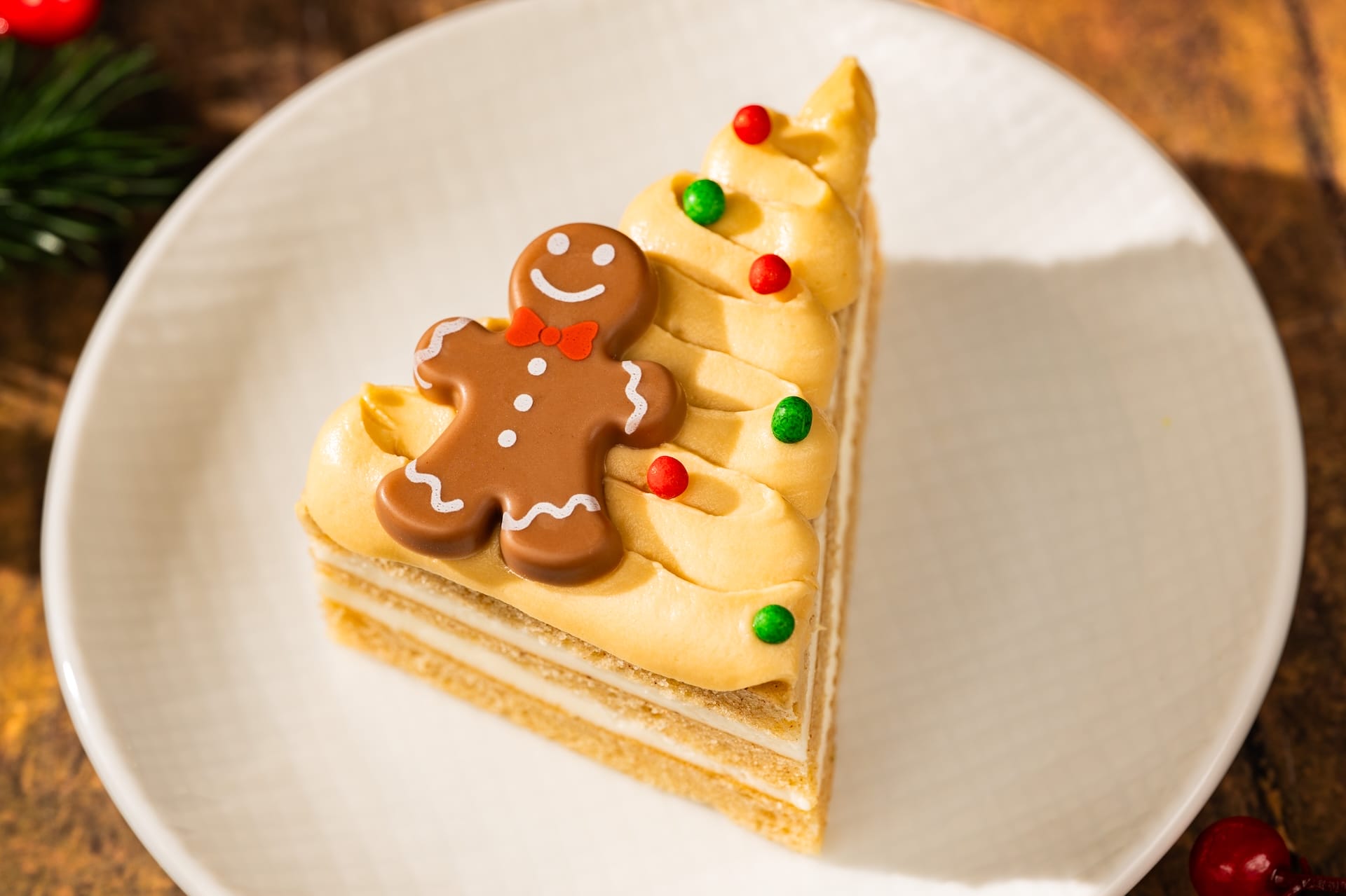 A slice of 2025 Holiday menu cake, topped with frosting, festive candies, and a gingerbread cookie—Disney Parks seasonal treat.