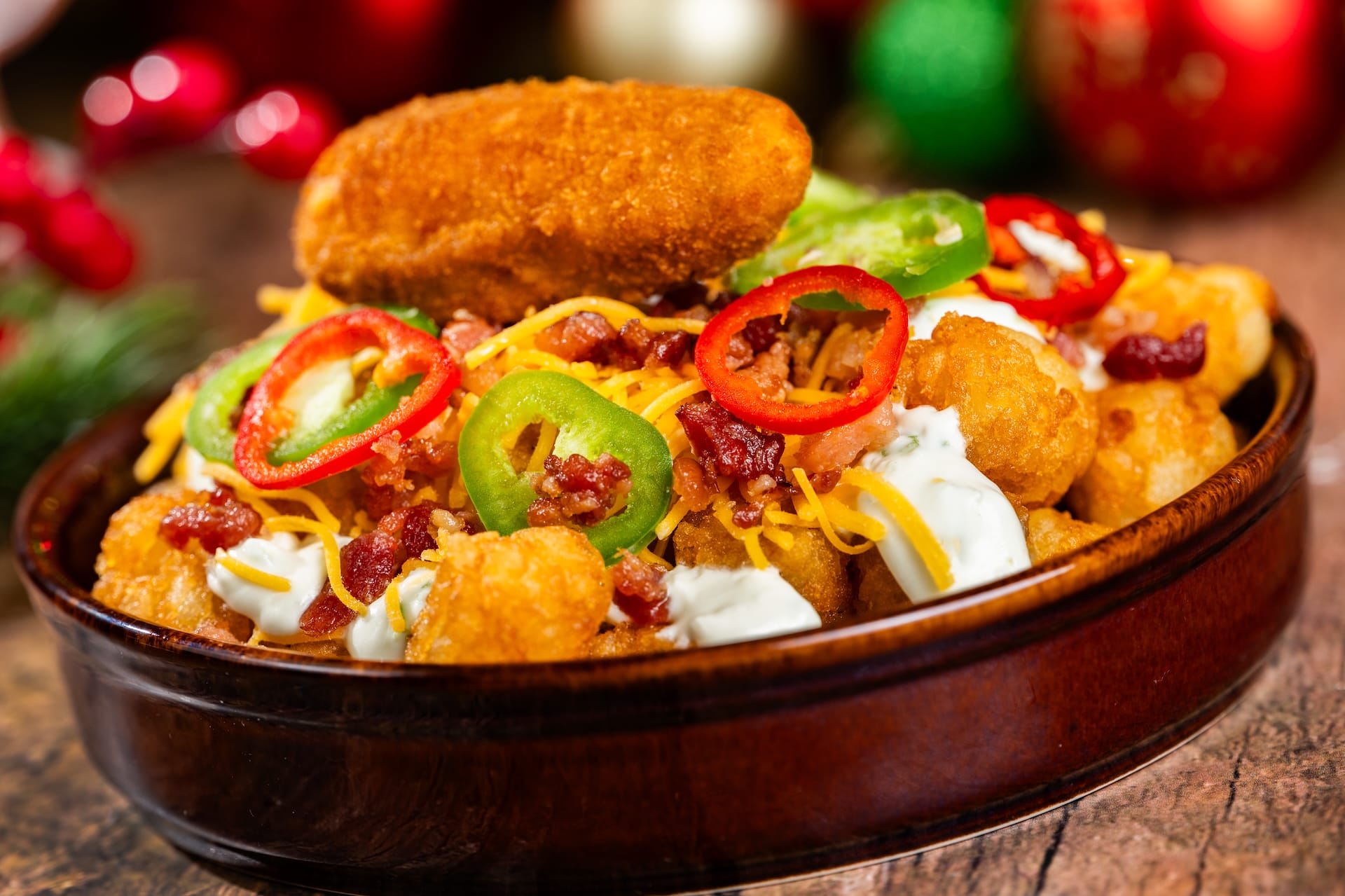 A festive Disney Parks bowl of loaded tater tots with cheese, bacon, jalapeños, and a 2025 Holiday Menu nugget.