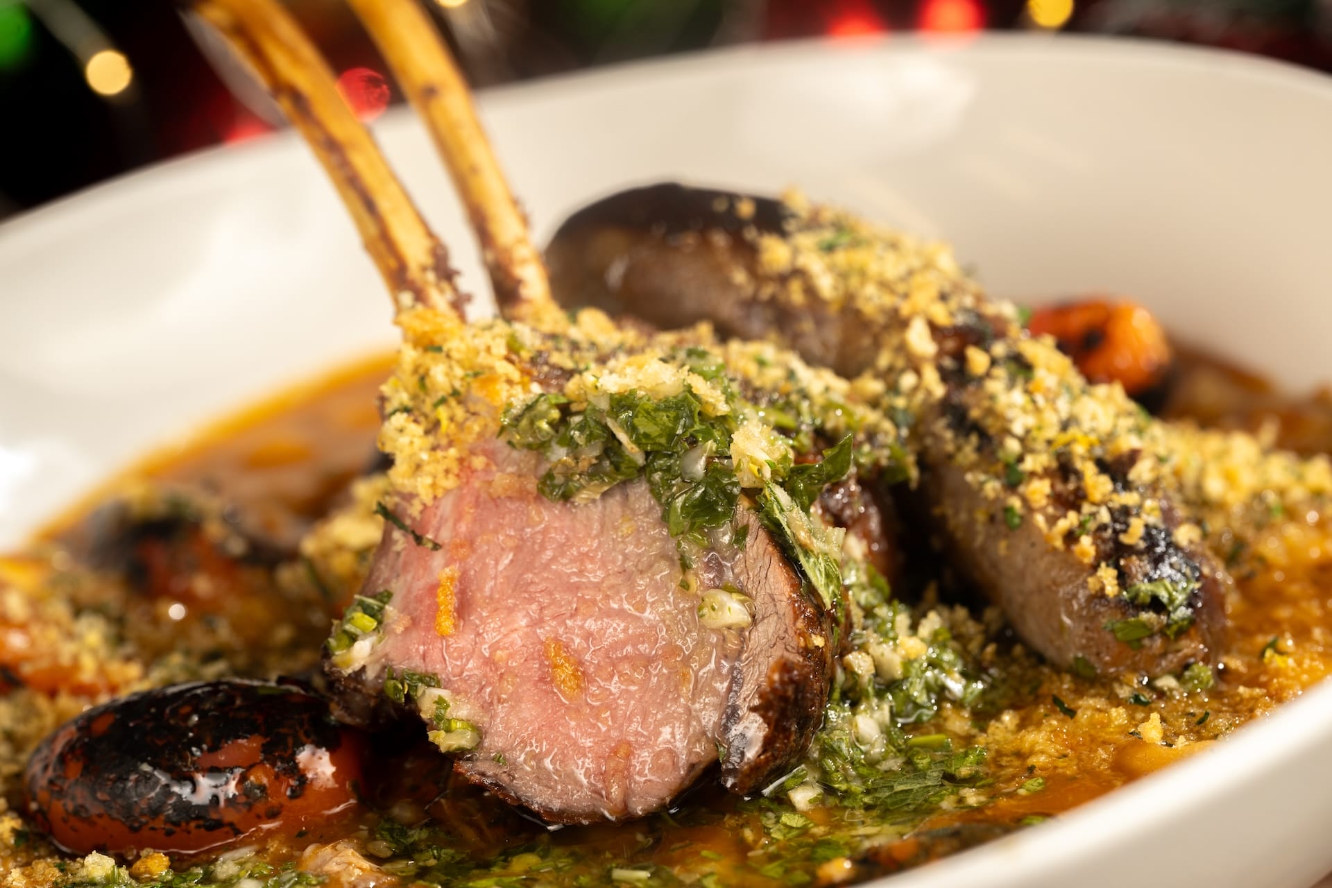 Holiday Menu’s herb-crusted rack of lamb with sauce, herbs, and veggies—plated with Disney flair like a fine castle feast.