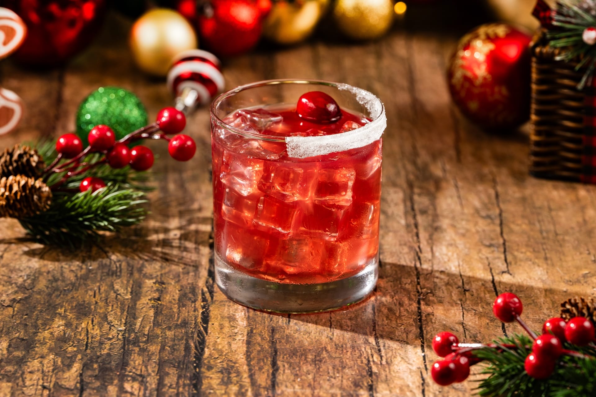 A festive red cocktail from the 2025 Disney Parks menu with cranberry garnish rests on a rustic table amid magical holiday decor.