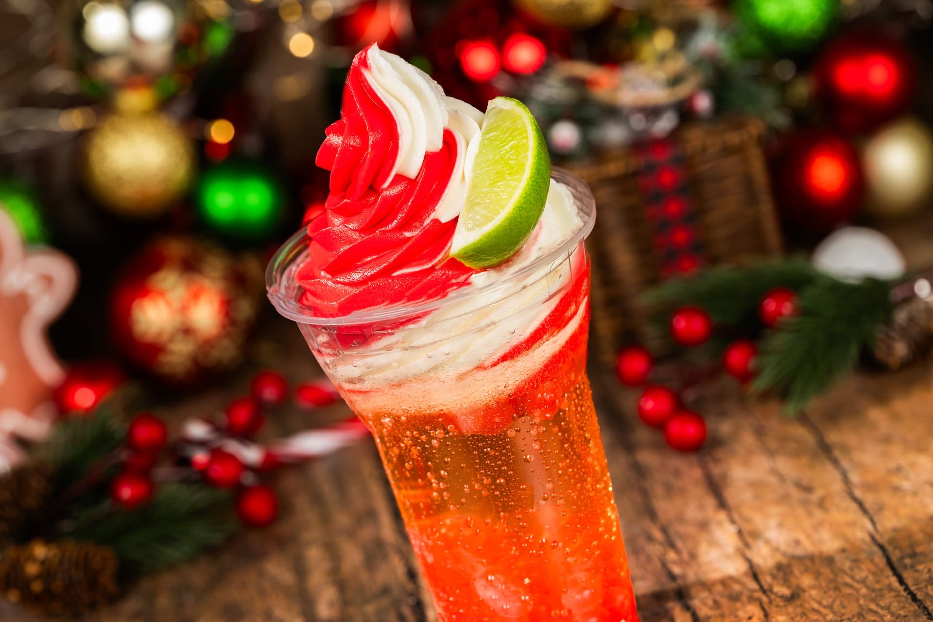 A cheerful holiday drink from the 2025 Disney Parks menu, topped with swirled whipped cream, lime slice, and festive decor.