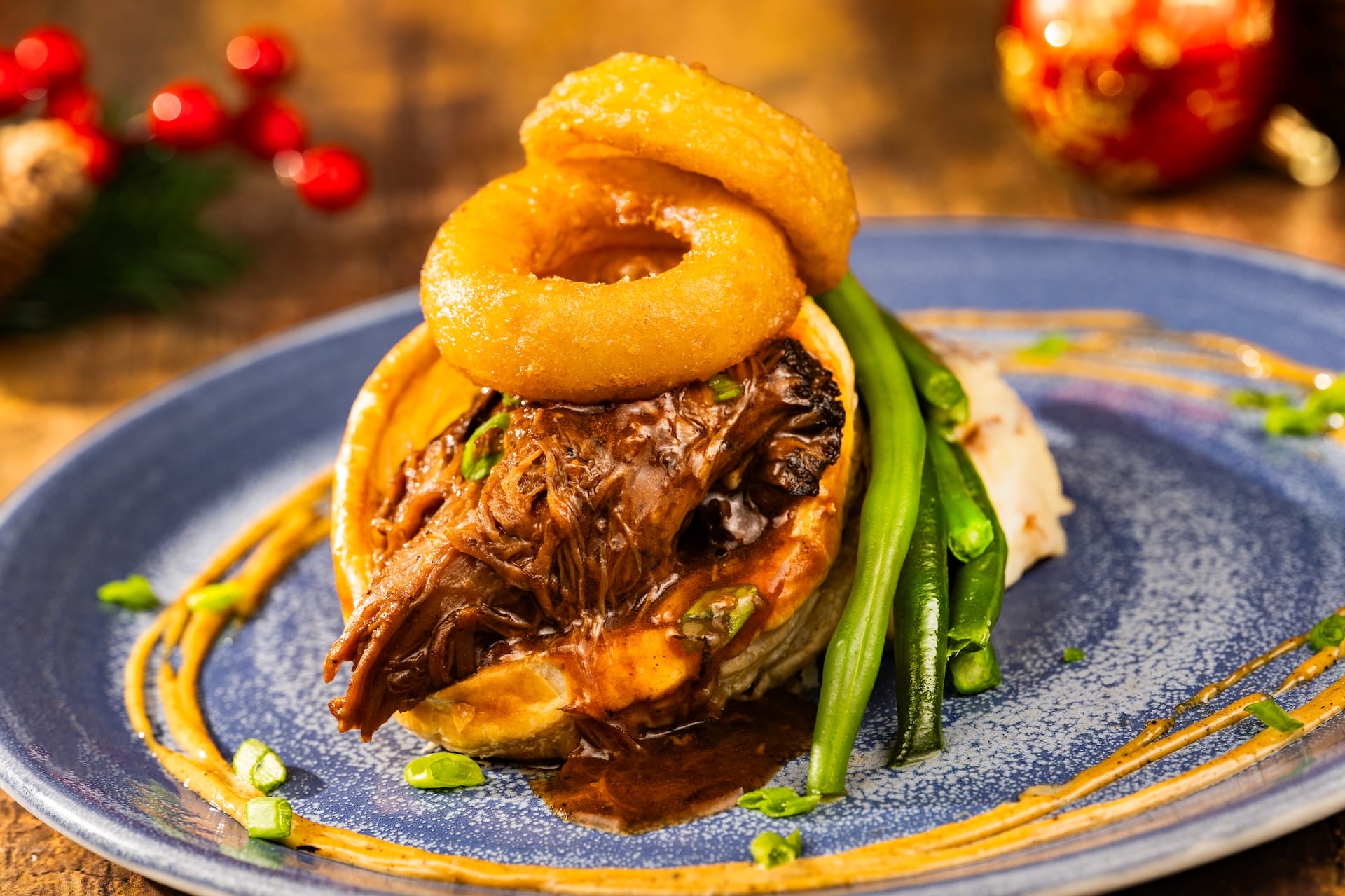 Festive braised beef with gravy, green beans, mashed potatoes, and onion rings from the 2025 Disney park menu, garnished with herbs.