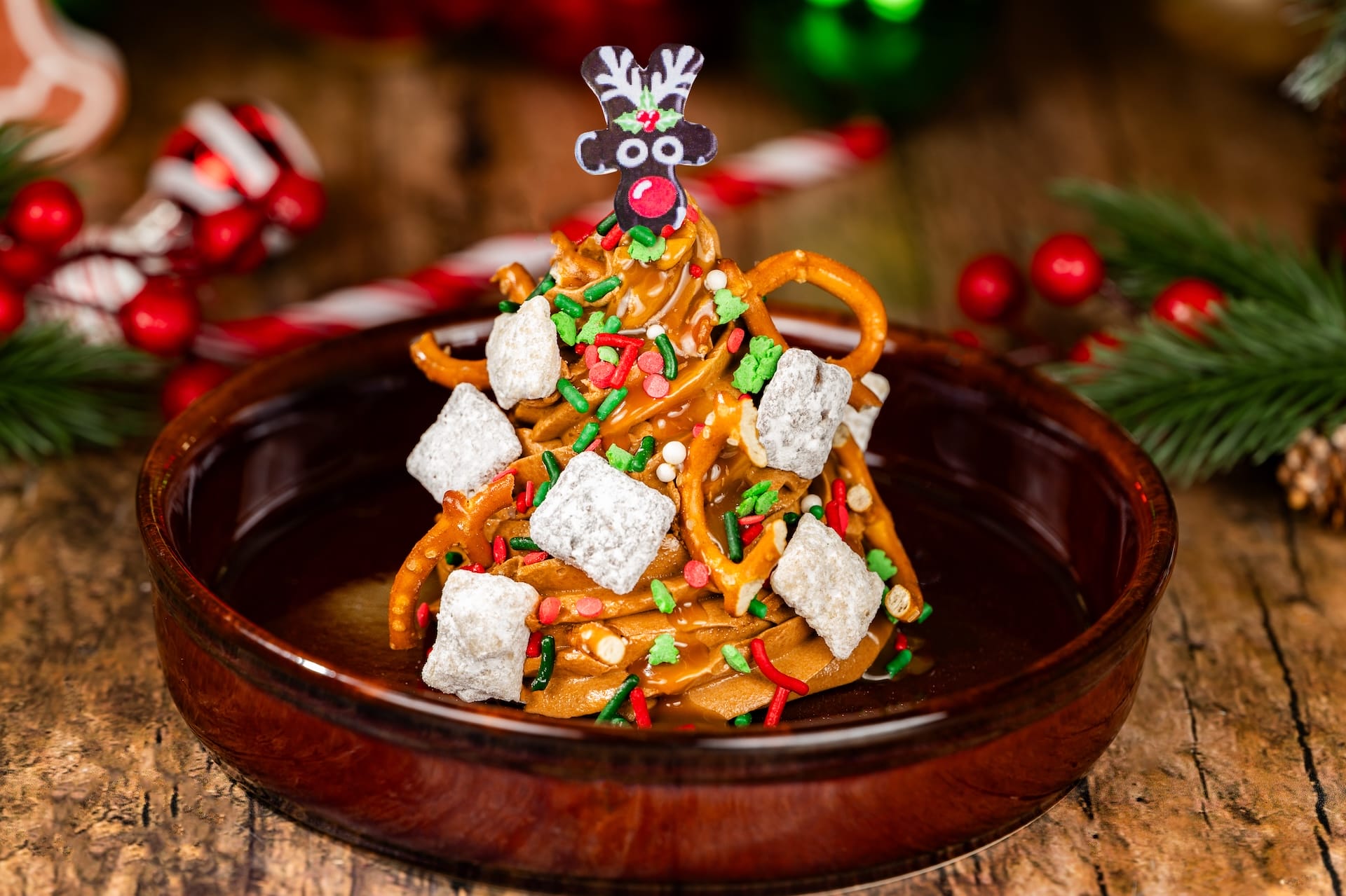 A Christmas tree-shaped holiday treat with pretzels, sprinkles, powdered sugar, and a reindeer topper—Disney park festive style.