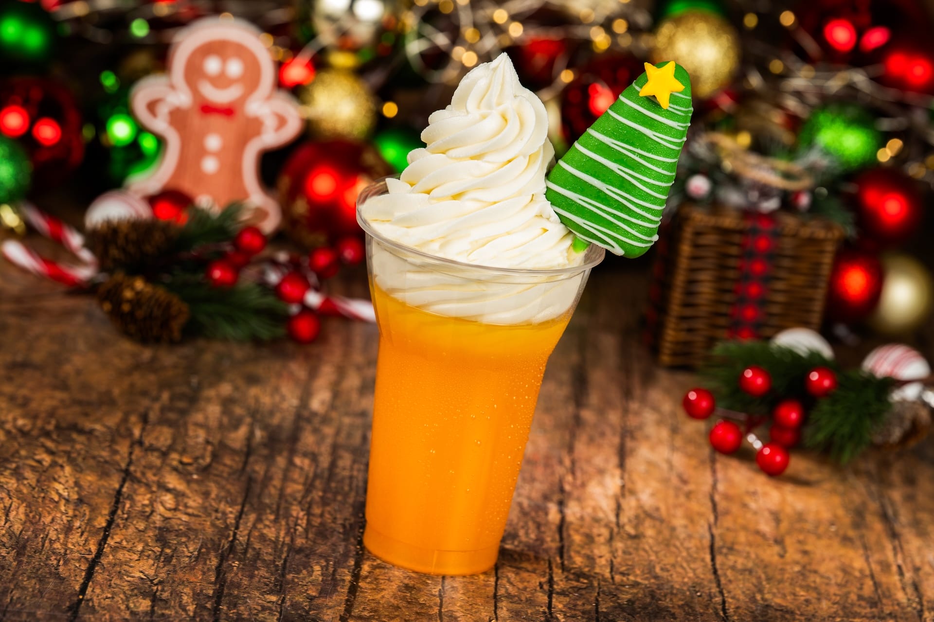 A festive orange drink from a Disney park Holiday Menu 2025, with whipped cream and a Christmas tree cookie on top.