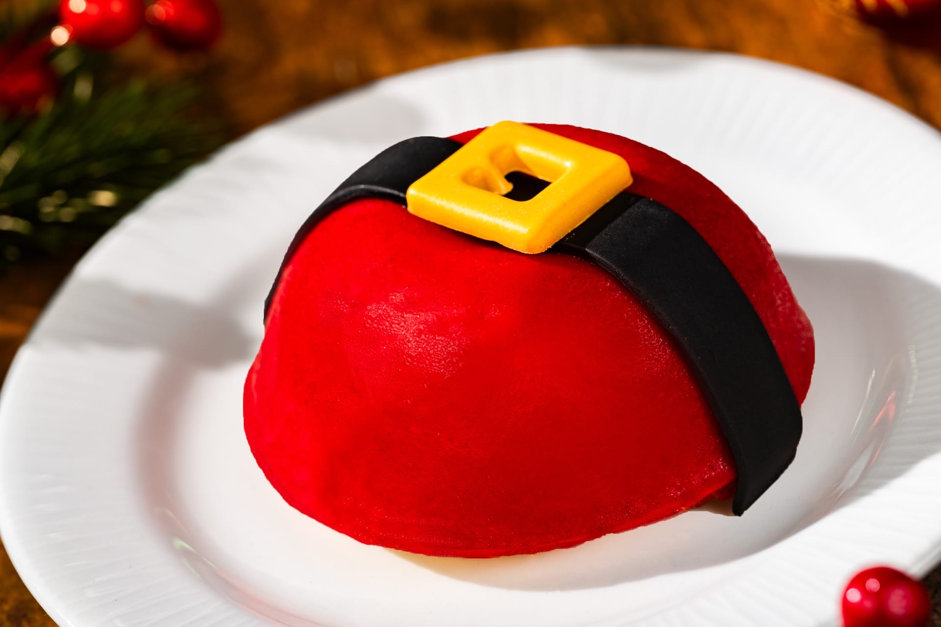 A round red Santa-inspired dessert from the 2025 Disney Parks menu sits on a white plate, resembling festive Disney treats.