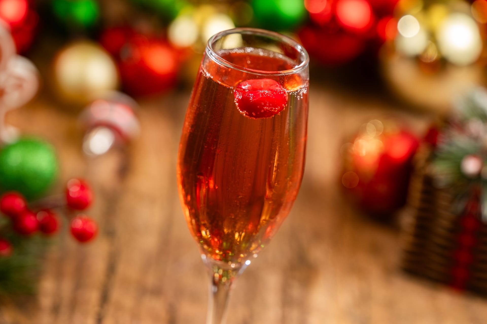 A festive champagne flute with a red sparkling drink, part of the 2025 menu at Mickey’s Very Merry Christmas Party in Disney Parks.