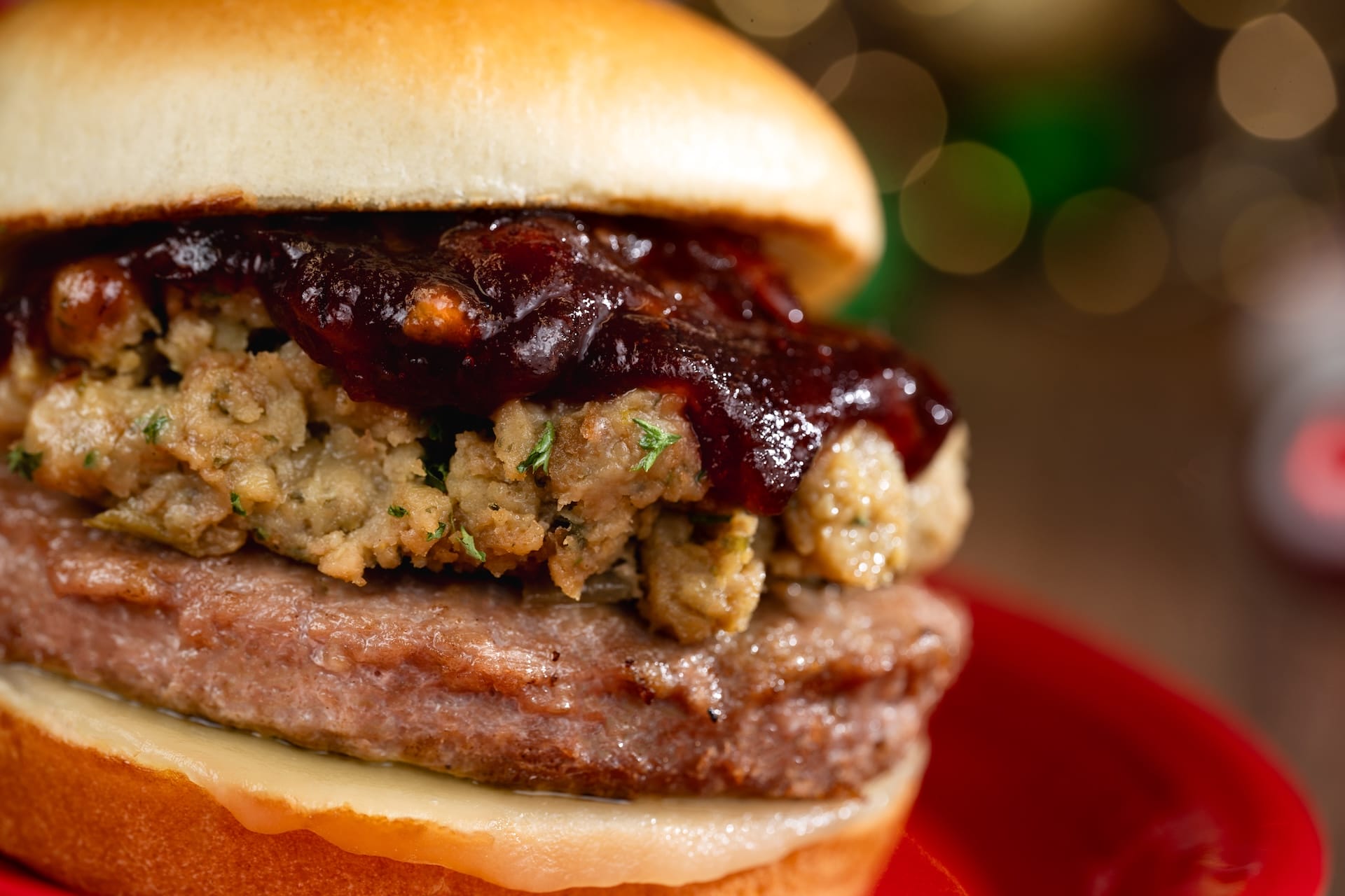 Festive Disney Parks 2025 burger topped with stuffing and cranberry sauce, served on a red plate—perfect for holiday magic.