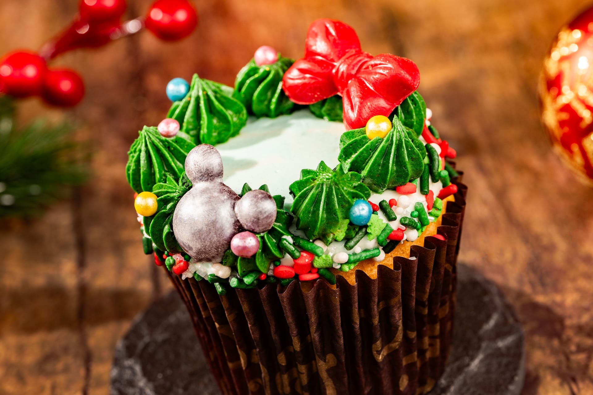 2025 Holiday cupcake with green icing, red bow, and silver Mickey candy—perfect for enjoying near any Disney castle worldwide.