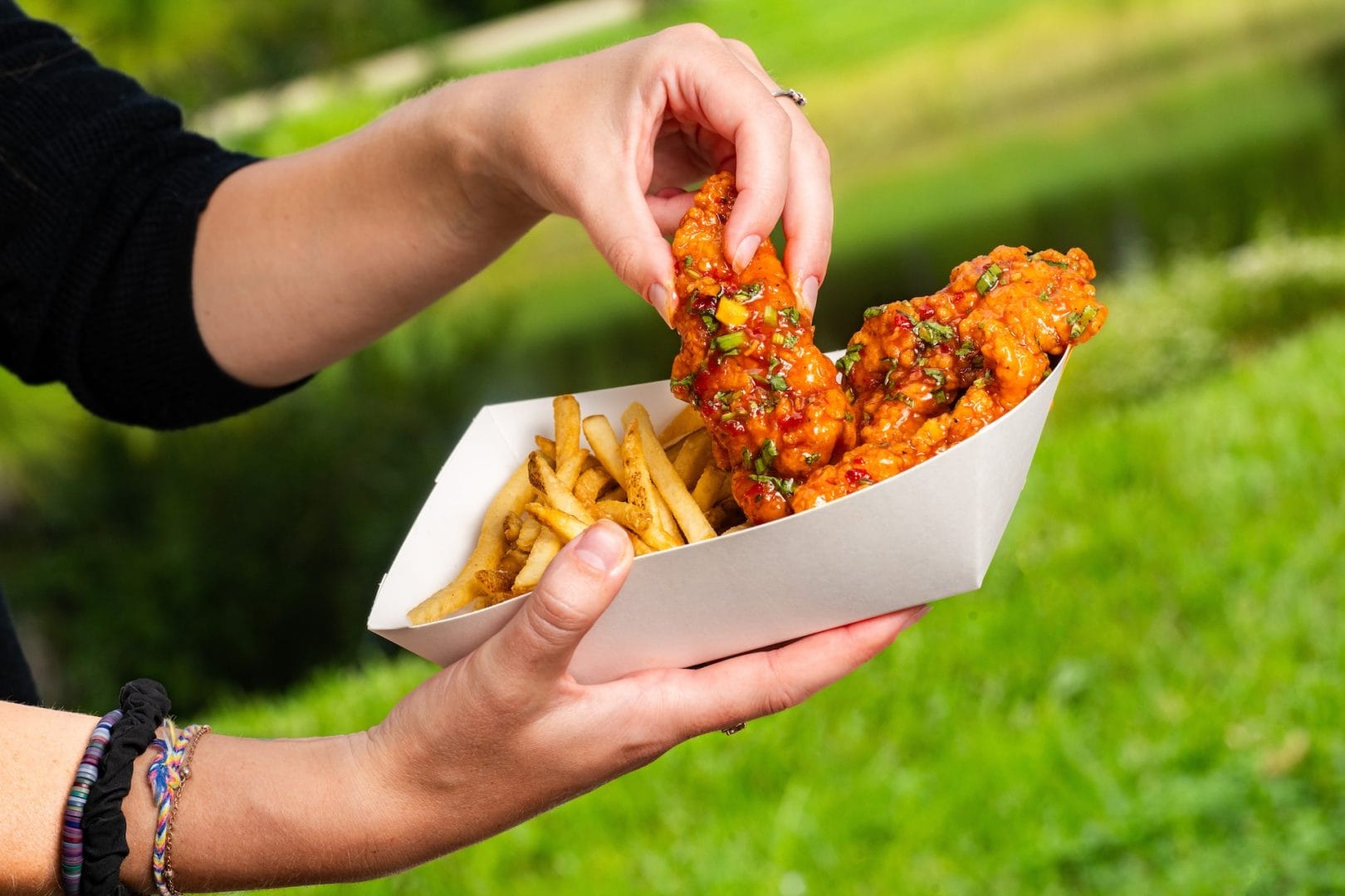 A person enjoys new Chicken Strips and fries outdoors at Disney World, picking up a tender with one hand.