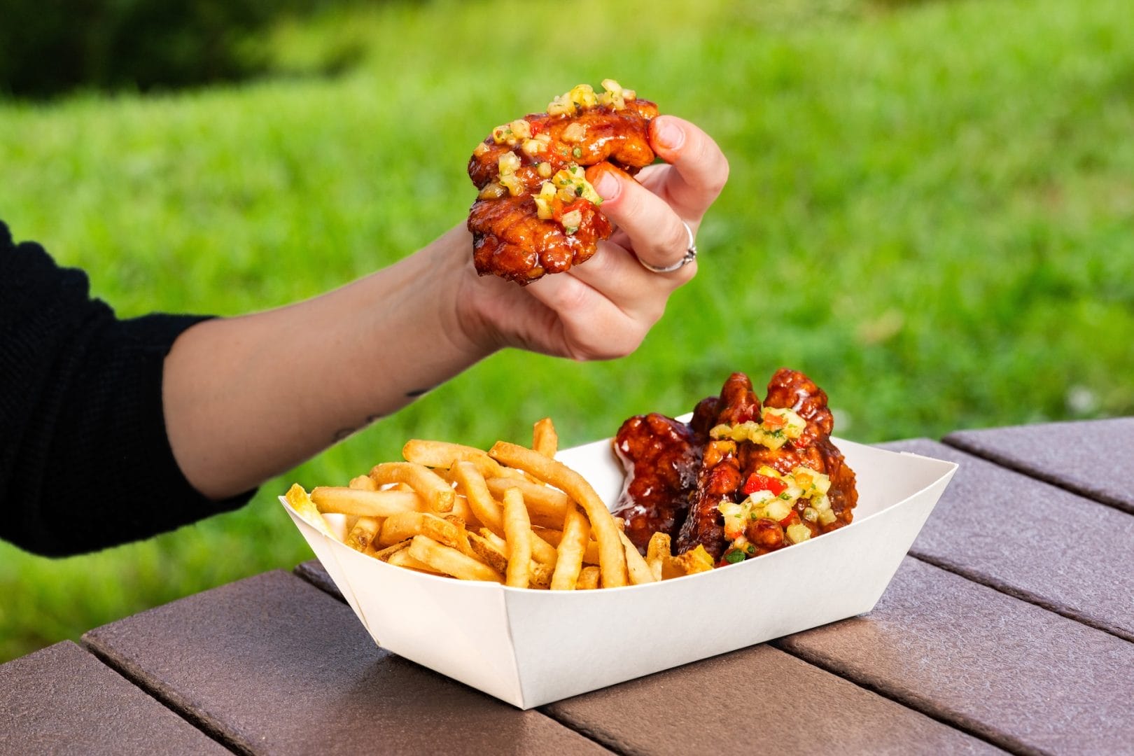 A hand holds sauced chicken strips with fries in a tray on an outdoor table at Disney World.