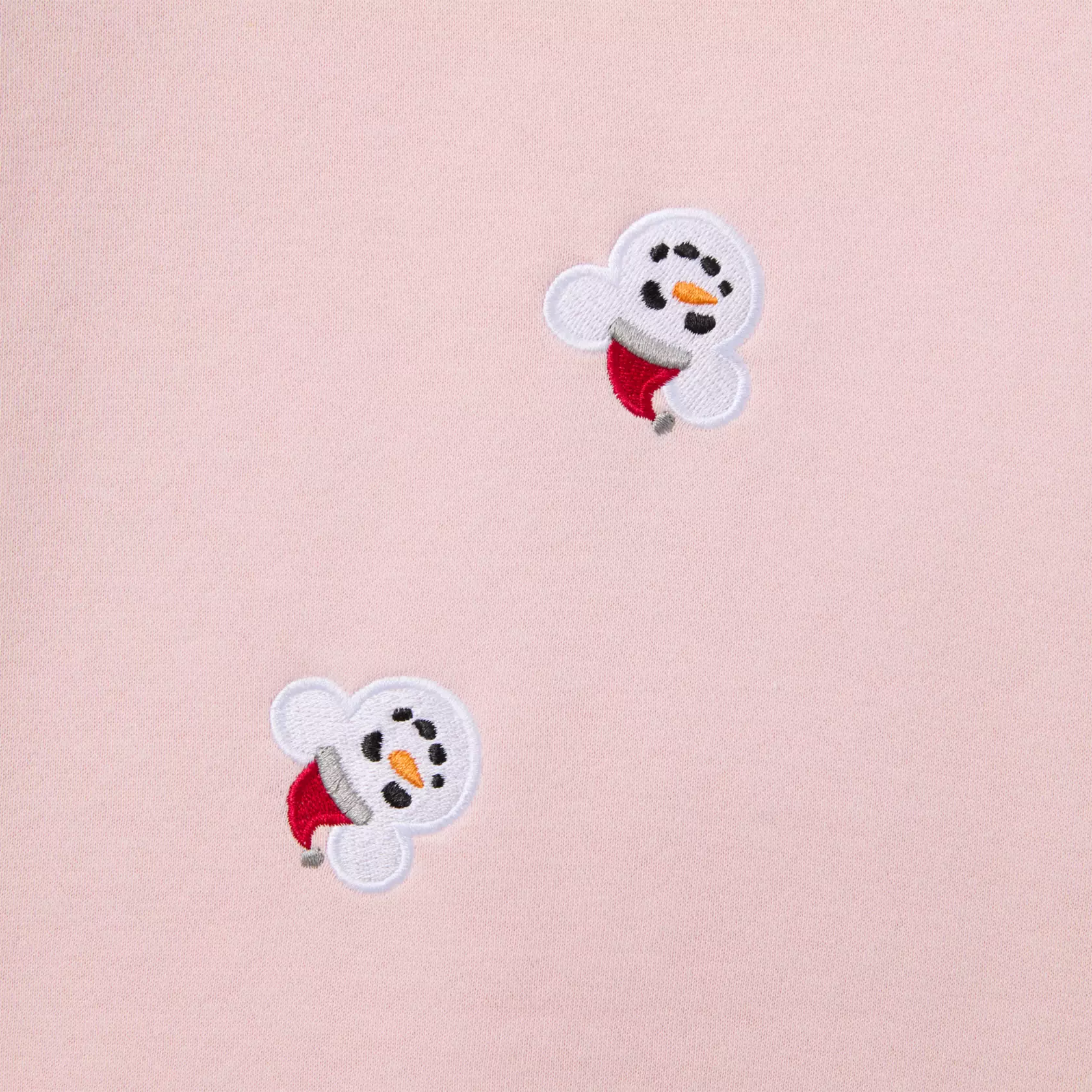 Close up of two small embroidered Mickey snowmen in red hats on a pink background.