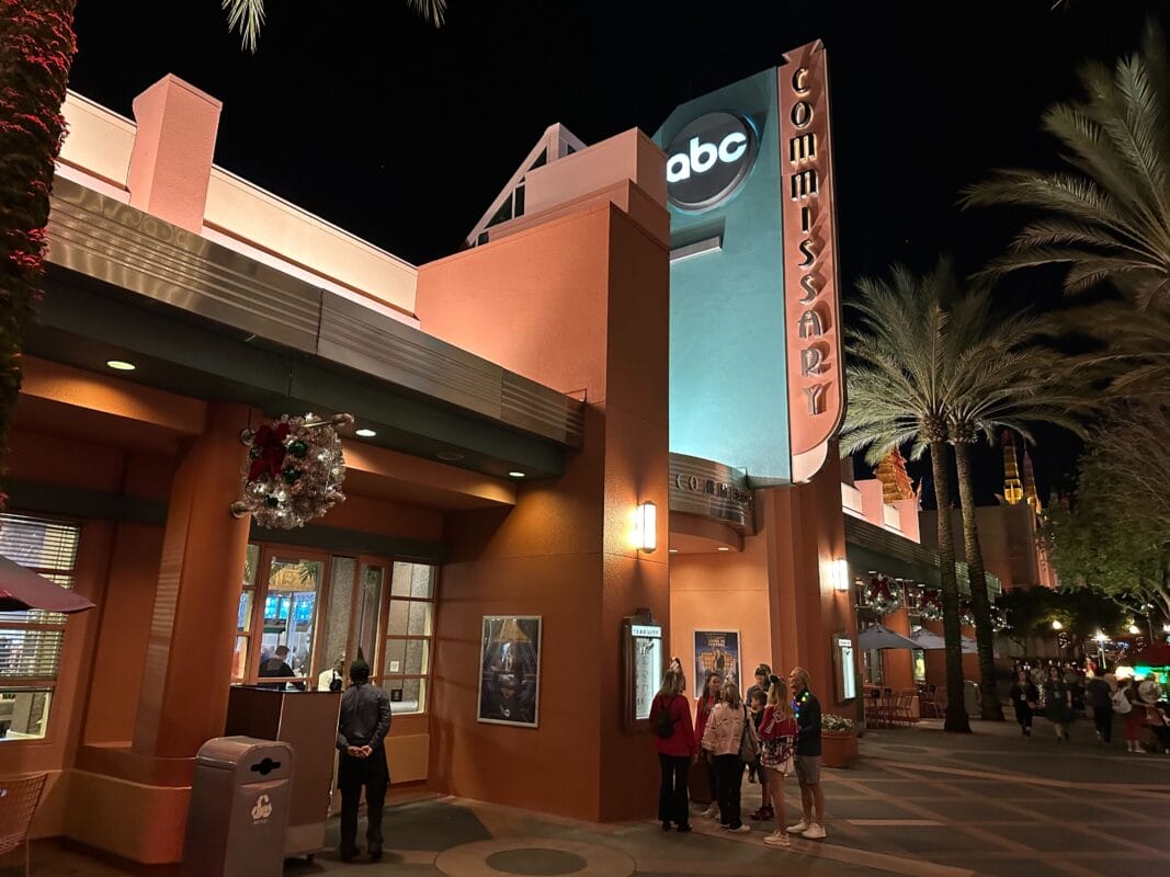 Guests gather outside the glowing ABC Commissary at Jollywood Nights in Disney’s Hollywood Studios, with palm trees and festive decor.