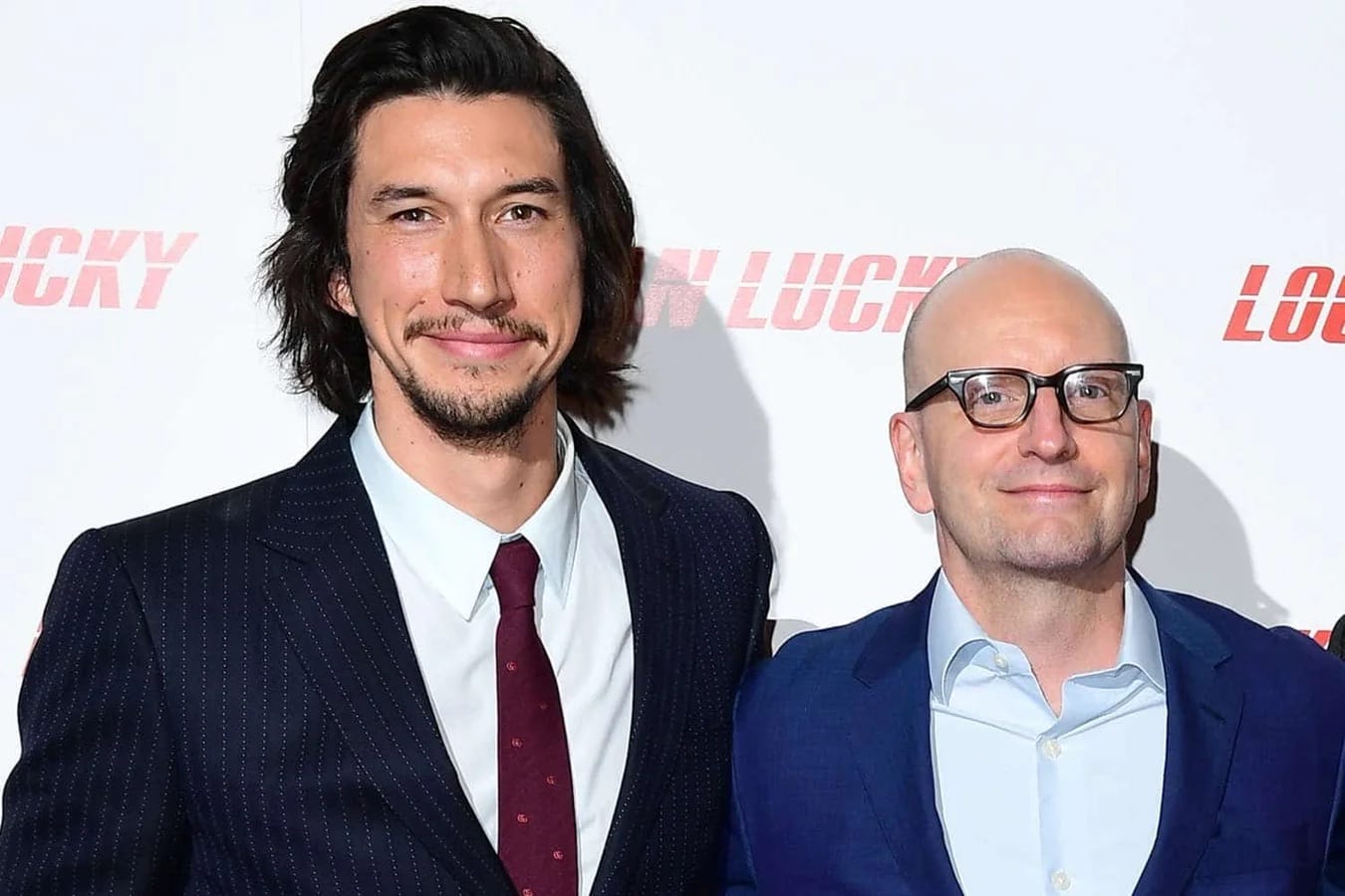 Two men in suits smile on a red carpet, reminiscent of VIP events at Disney Parks, though not in front of any Disney castle.